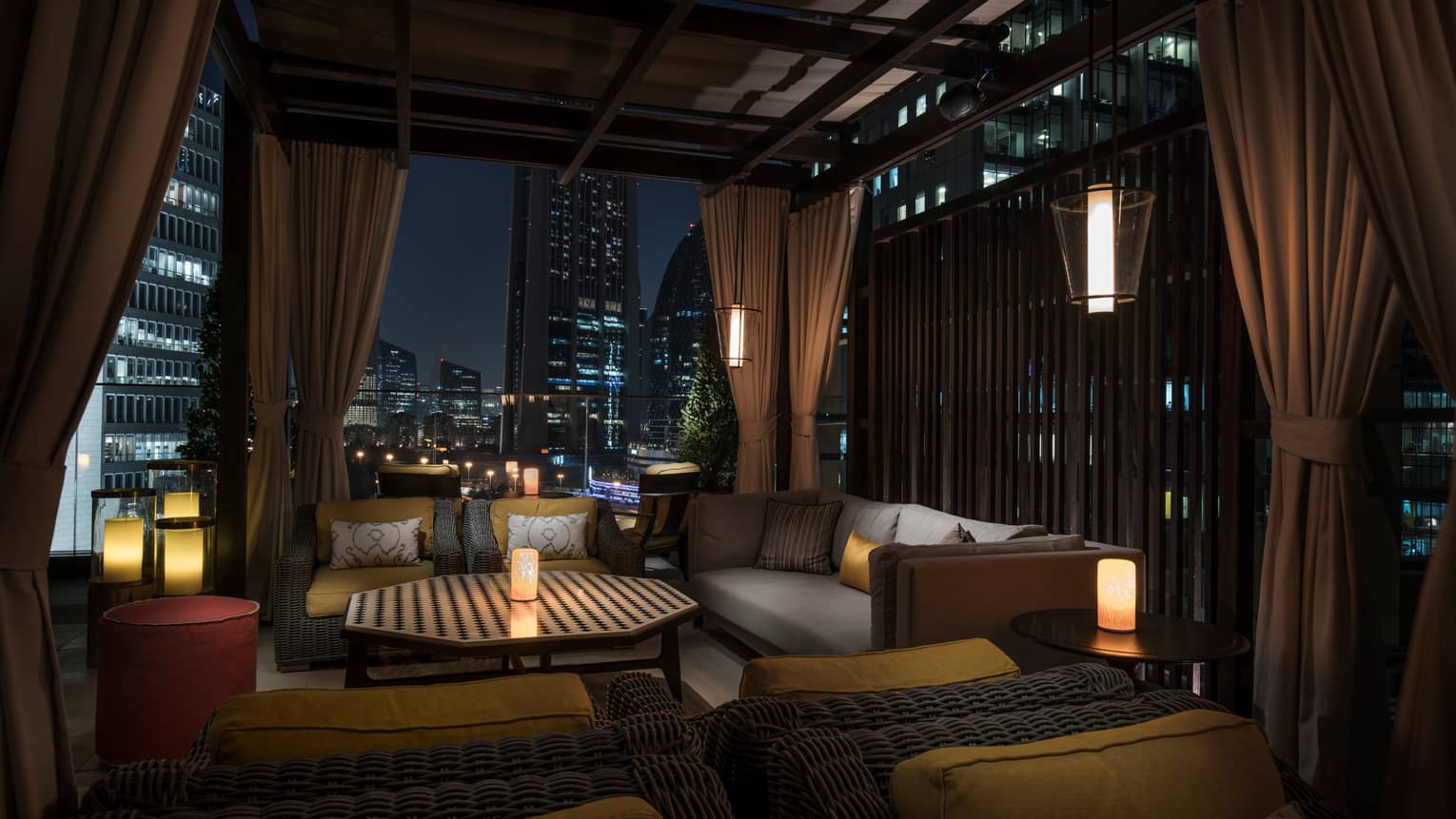 Outdoor patio lounge area at night with candles, plush cushions, wood roof