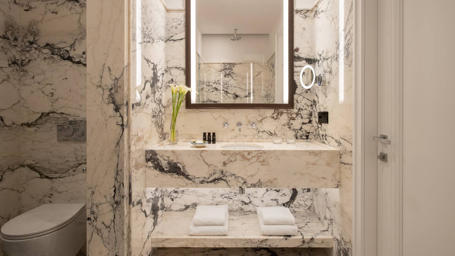 Bathroom with black and white marble walls and vanity, illuminated mirror, separated toilet room