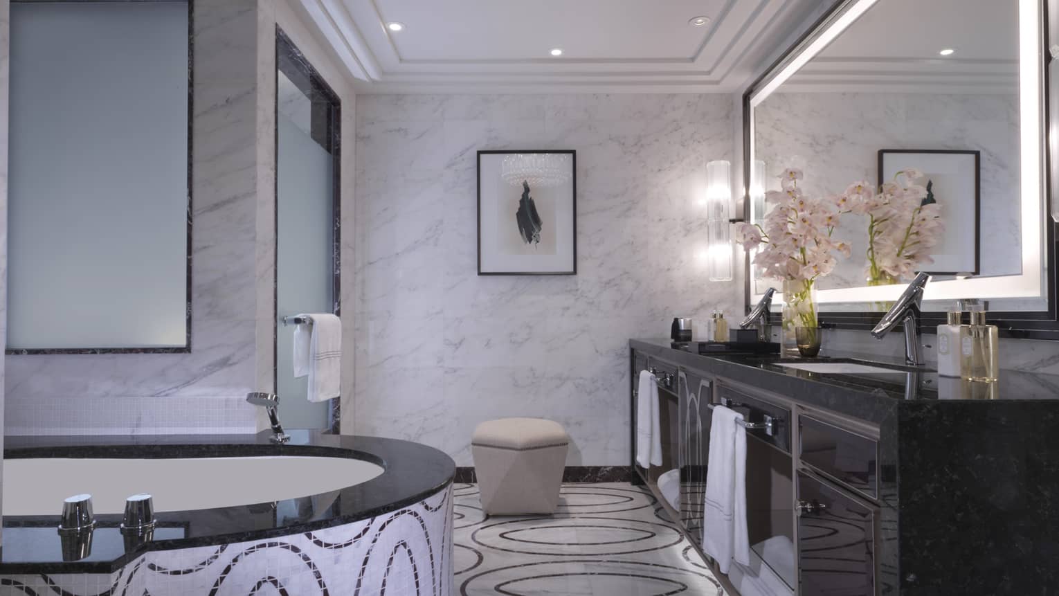 Luxurious marble bathroom featuring a soaking tub with mosaic details, black granite vanity, elegant lighting and orchid floral accents