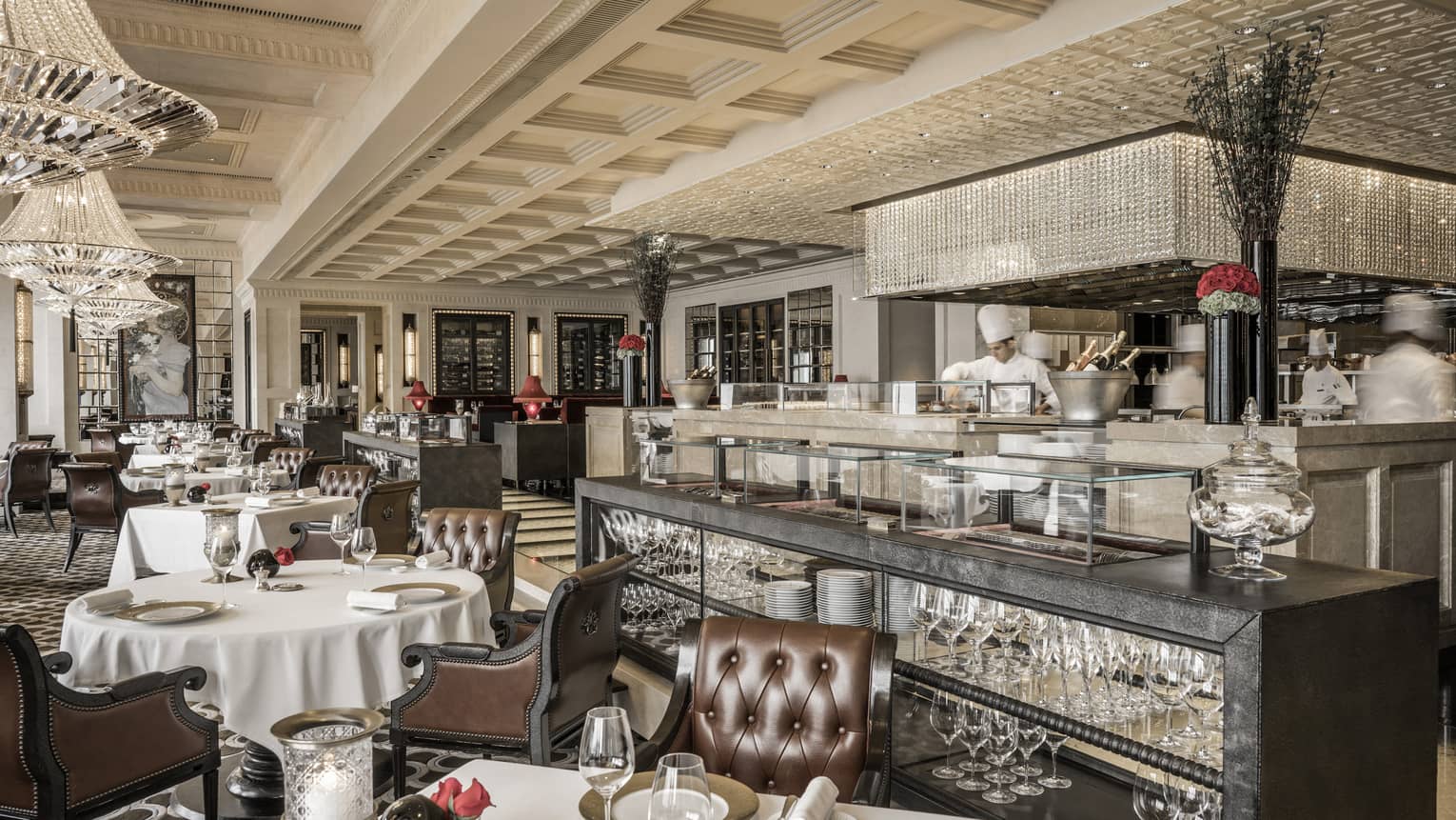 Contemporary chinoiserie dining room tables, leather chairs, chefs behind marble counter with crystal overhang 