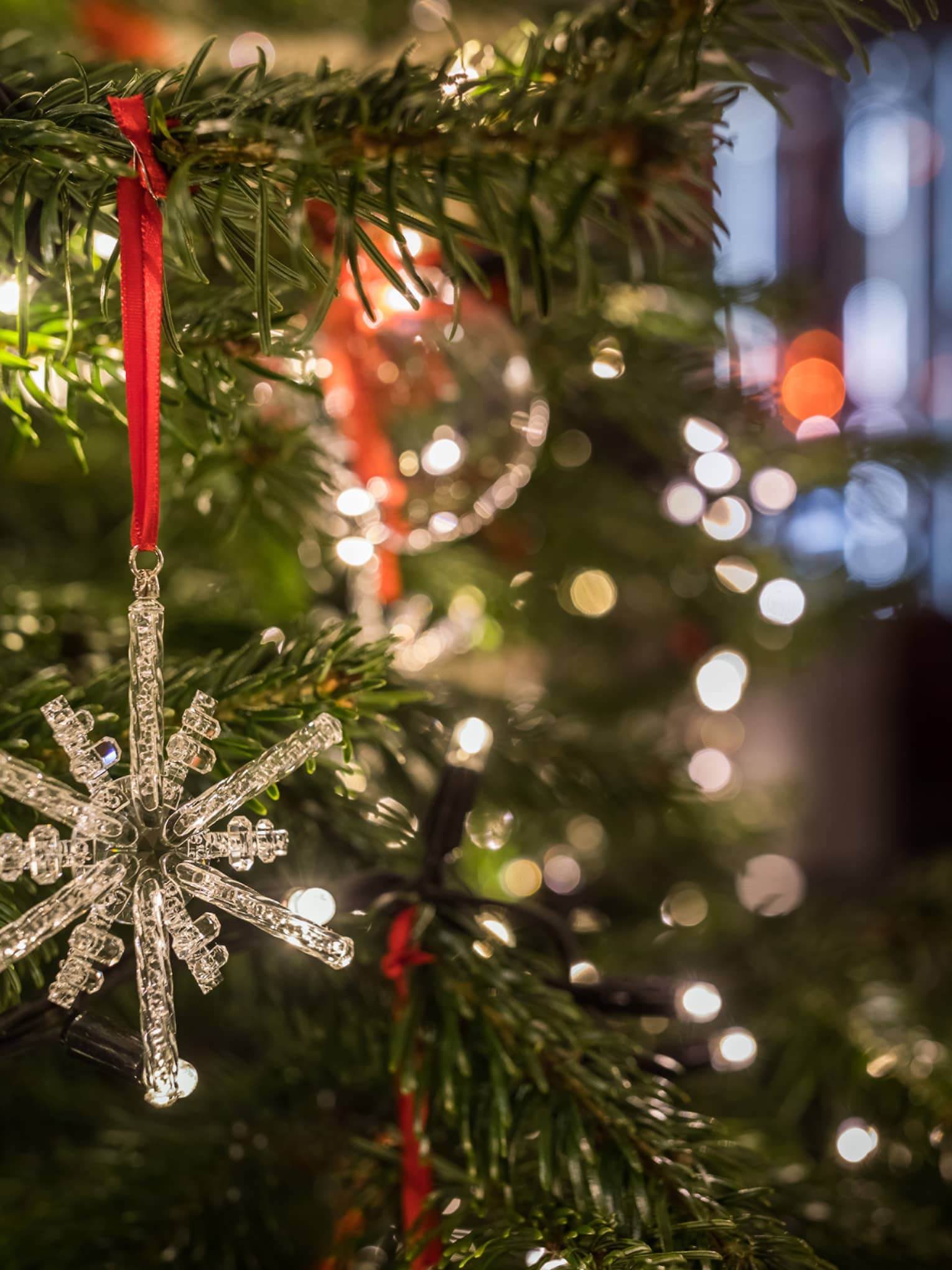 Close-up of a crystal snowflake ornament hanging on a Christmas tree with festive lights in the background