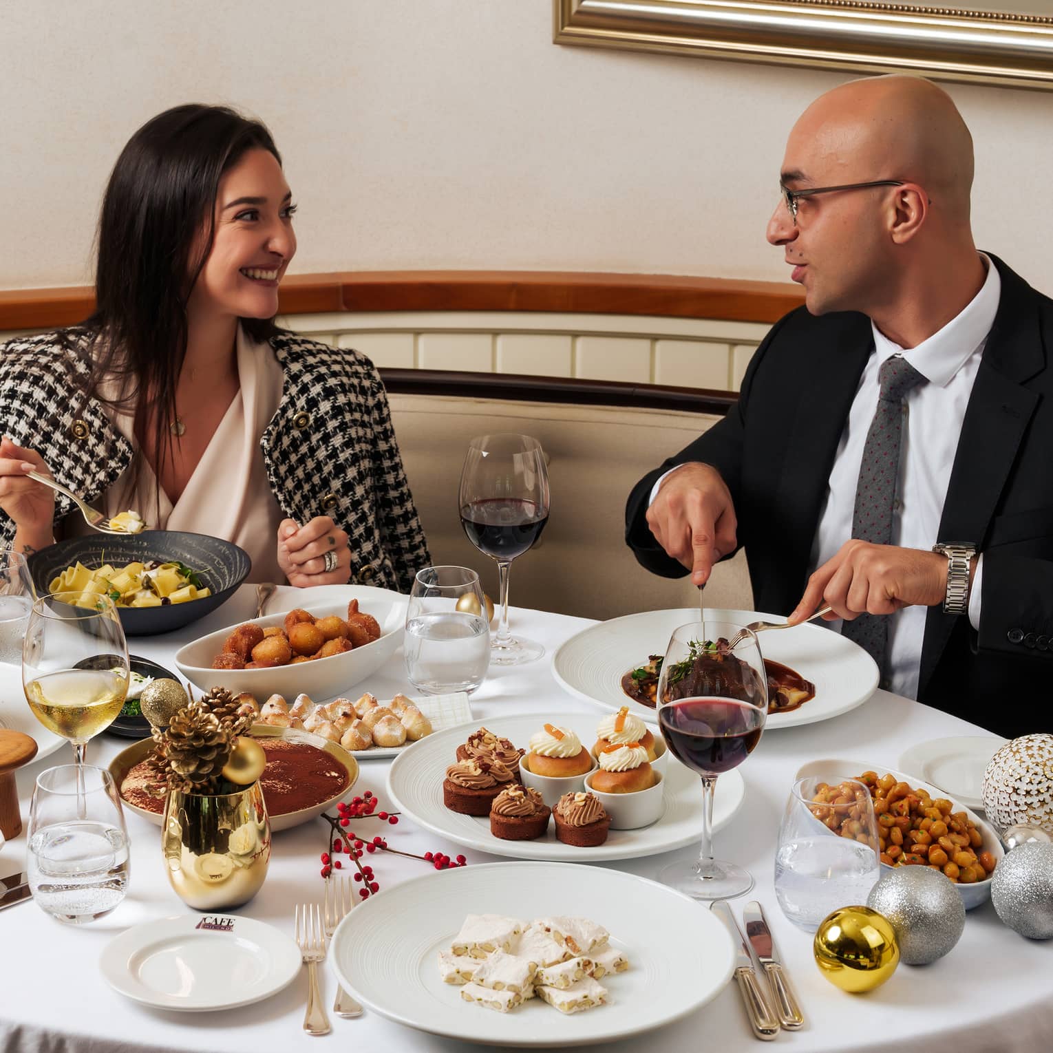 Two people dressed in eventing attire sit at a table filled with festive dishes