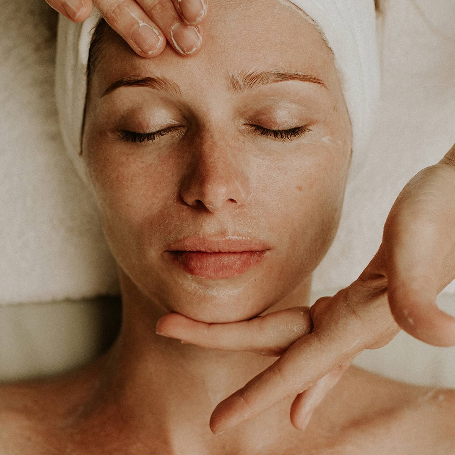 Person receiving a relaxing facial massage with eyes closed and head wrapped in a towel