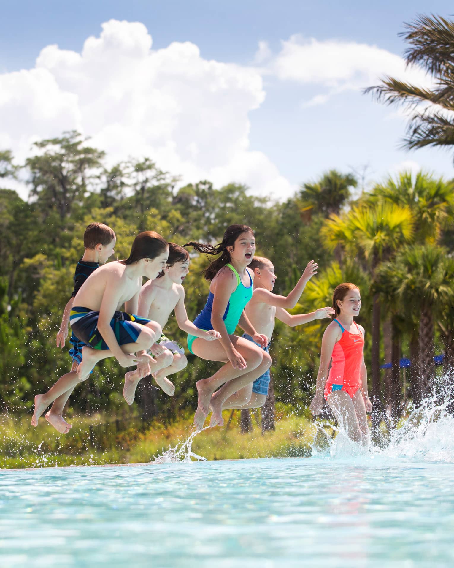 Group of children wearing swimsuits jump into outdoor swimming pool