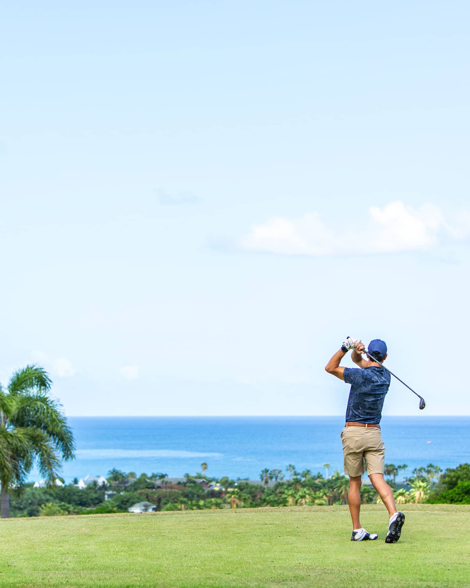 ,A man playing gold near palm trees and and ocean.