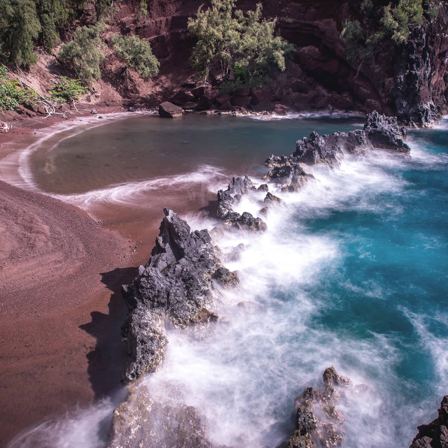 A red sand beach with waves crashing onto the sand.