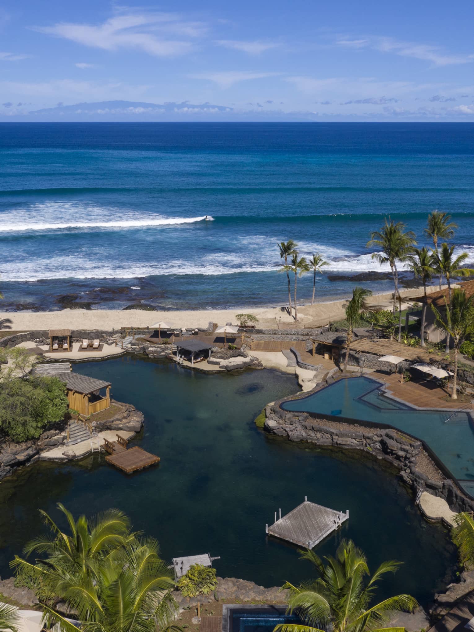 Aerial view of resort pool that mimics a curved pond, palm trees, beach and ocean