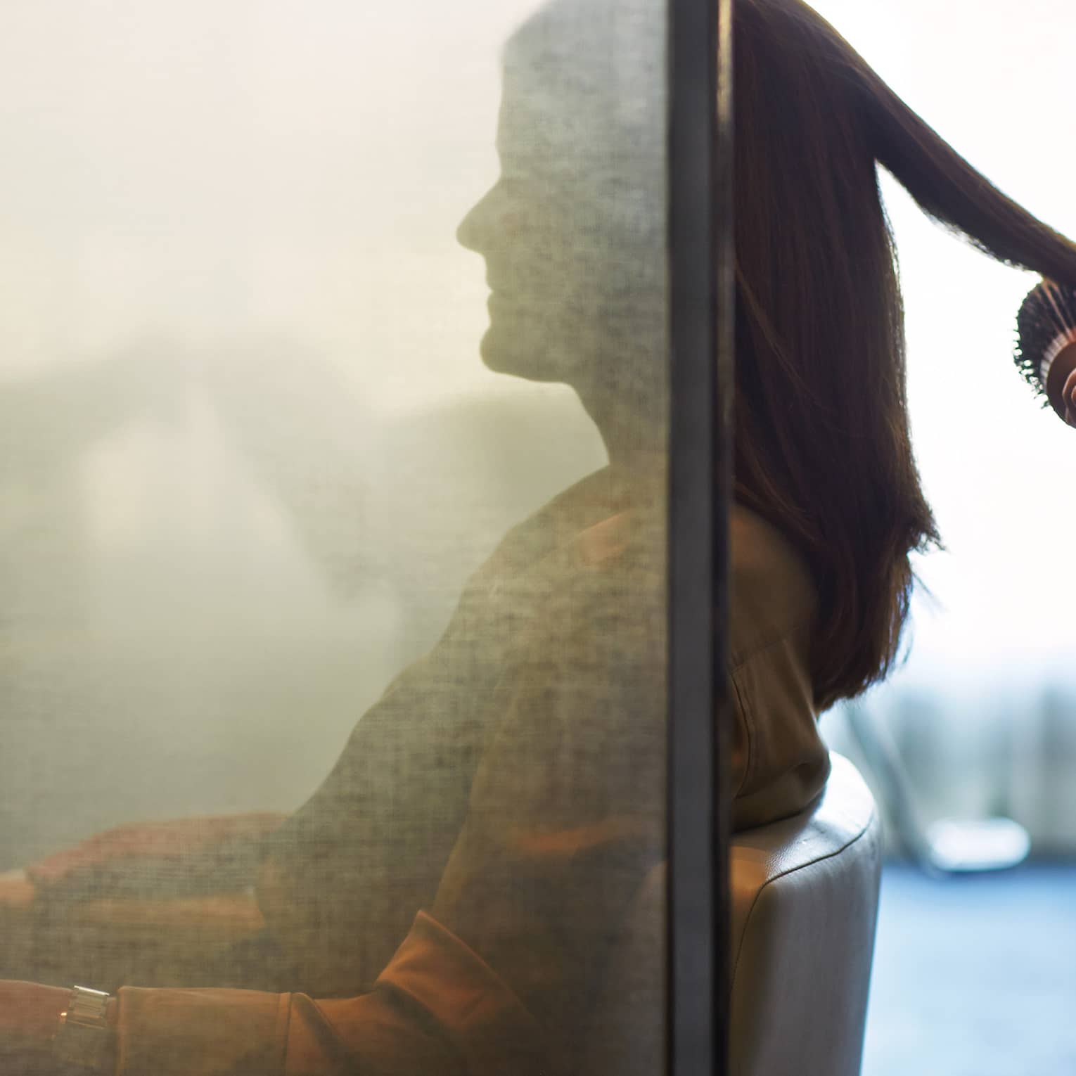 Silhouette of woman behind salon screen as hairdressers brushes, blow dries hair