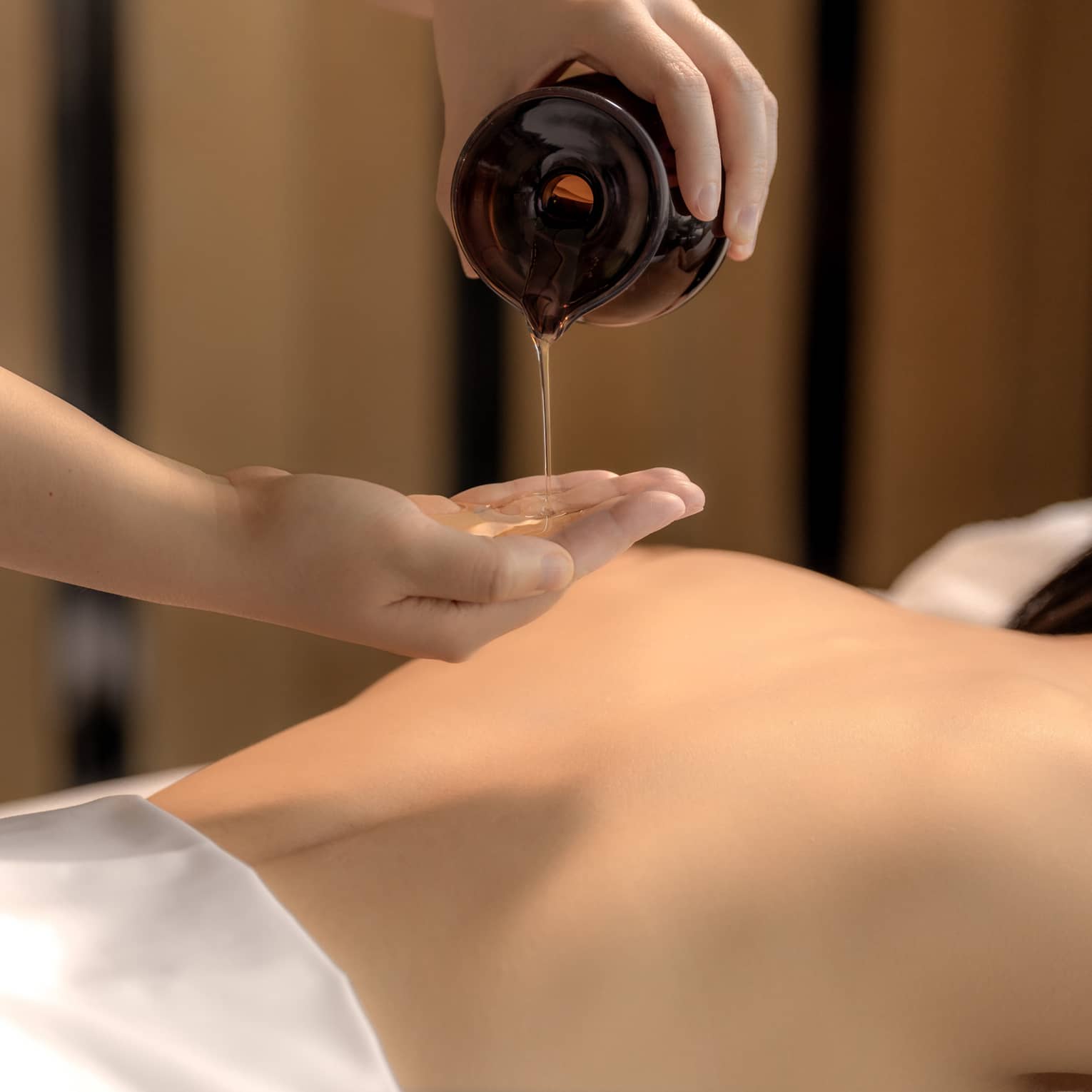 Spa therapist pours oil into hand above woman?s bare back in preparation for a massage