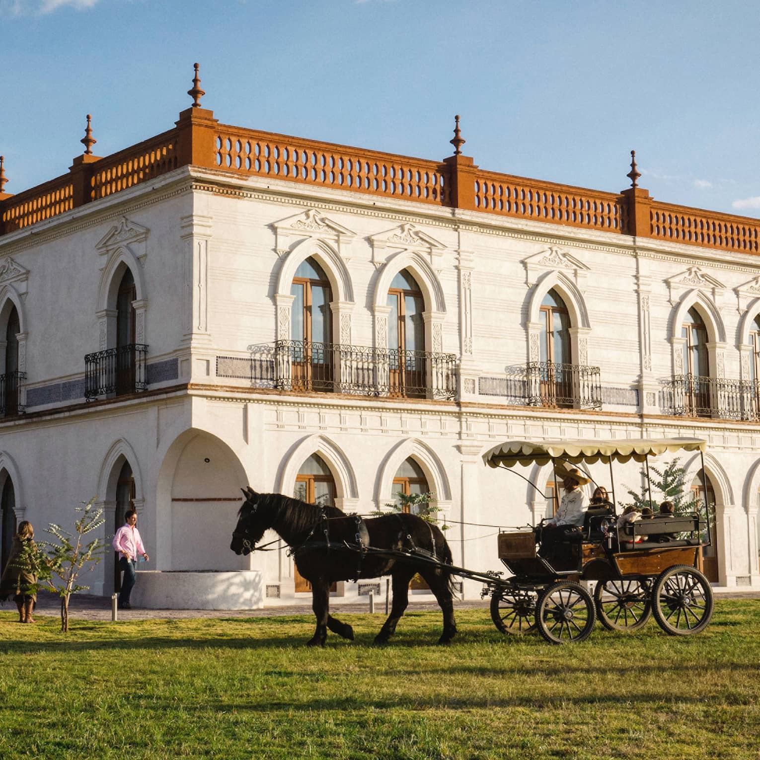 Guests enjoying a horse-drawn carriage ride around a large white building with several beautifully carved arched doorframes.