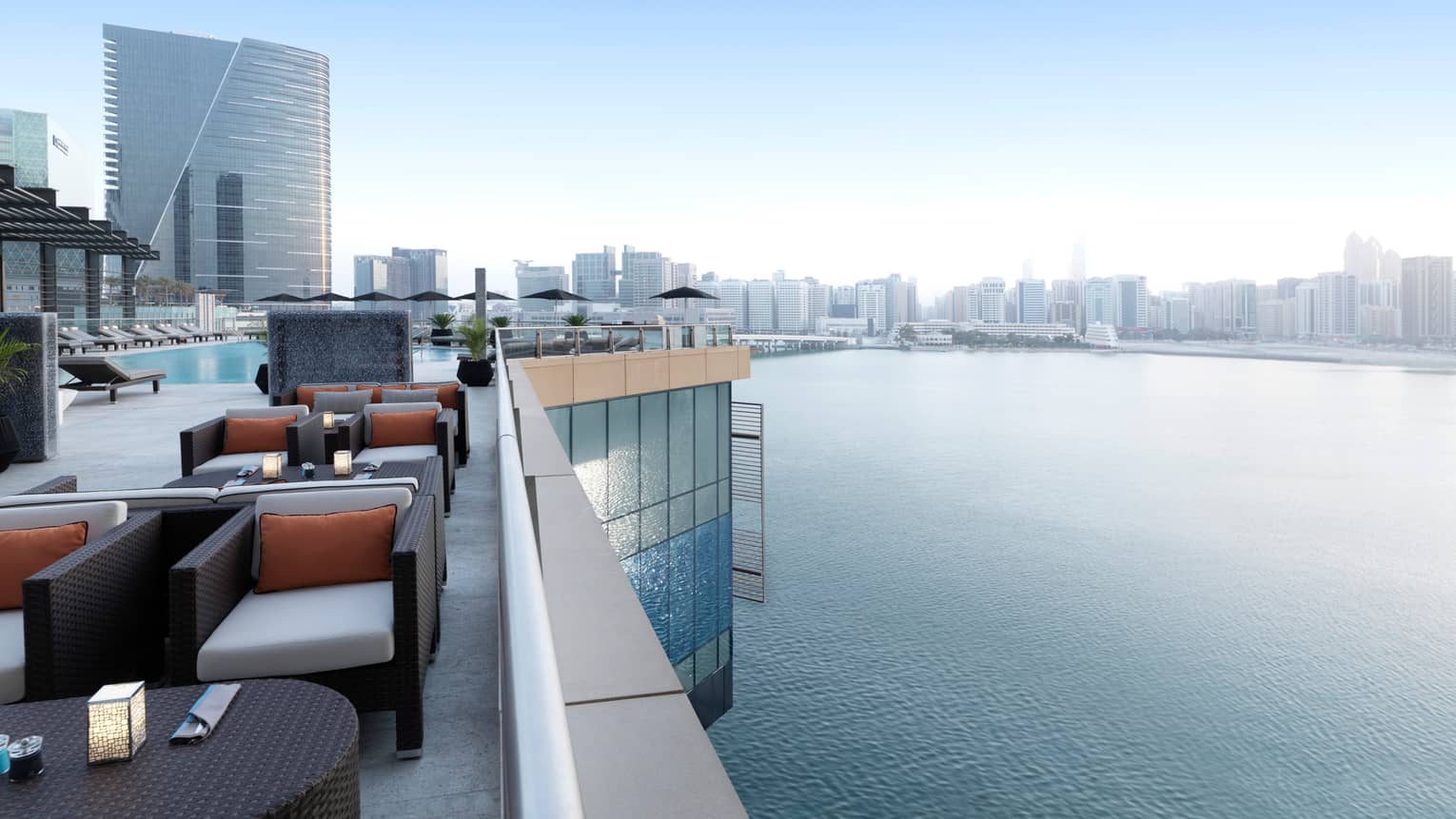 Rooftop lounge with stylish black wicker armchairs, cushions, candles on tables, swimming pool, overlooking Arabian Gulf