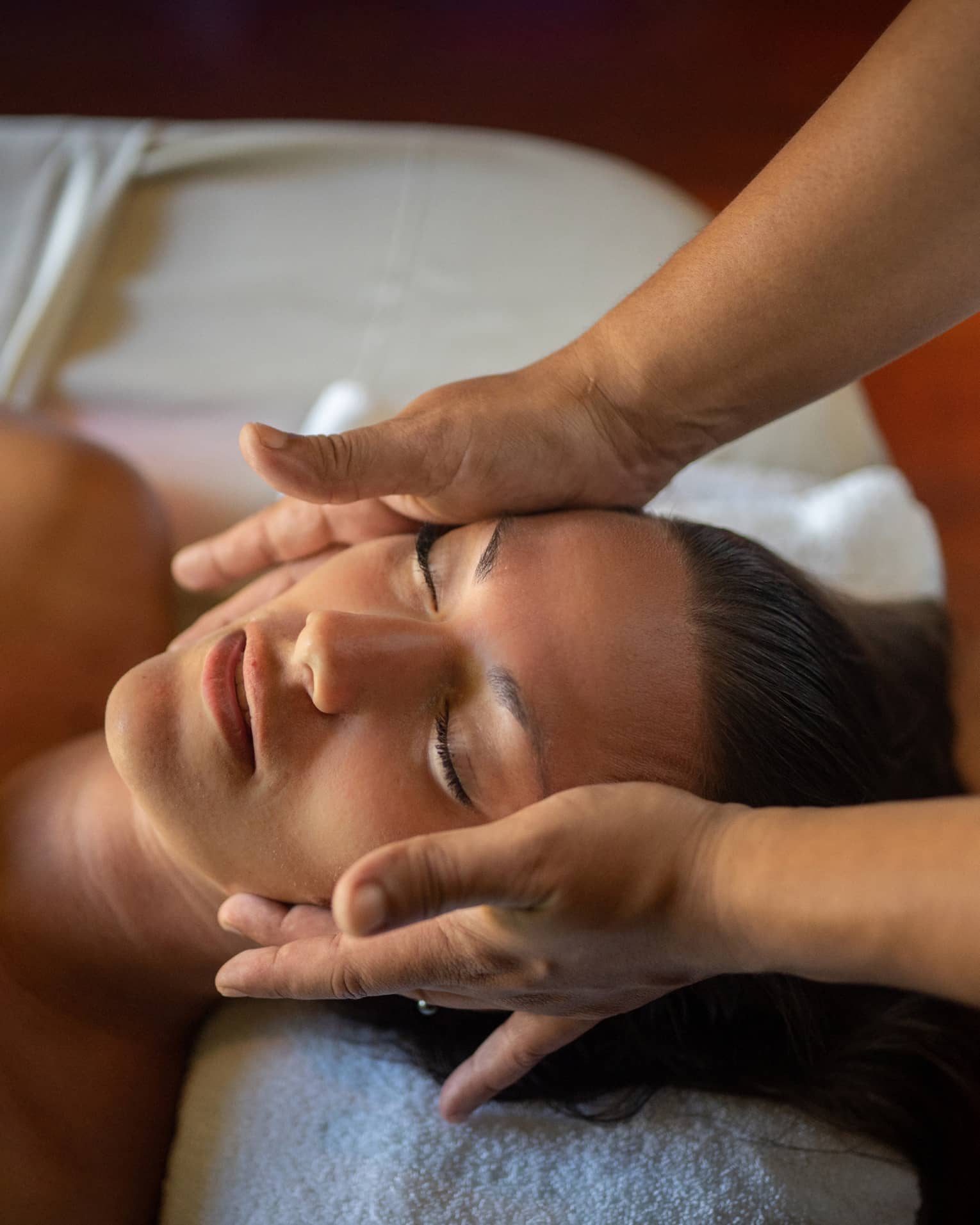 Woman lays on massage table with eyes closed as hands massage her cheeks and chin