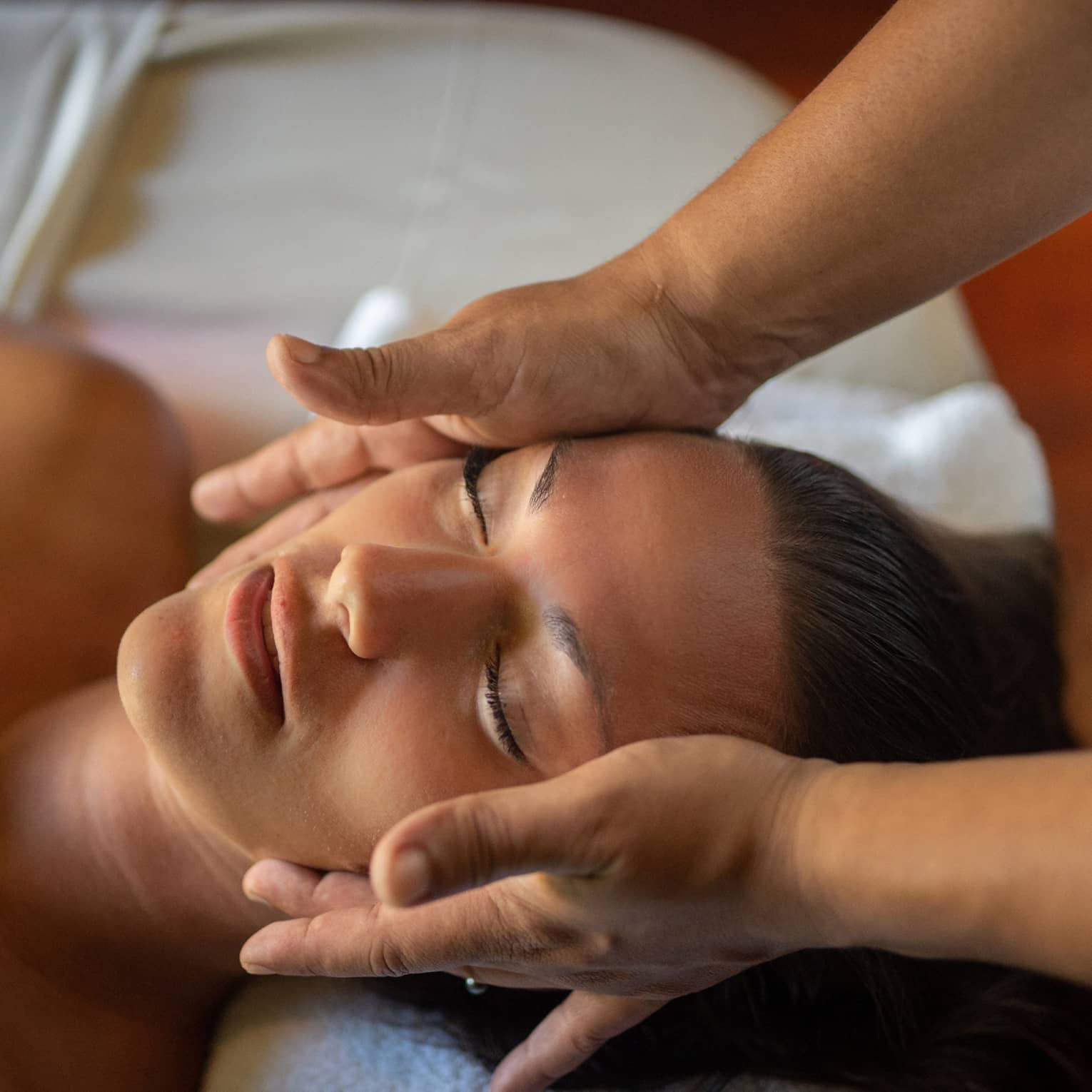 Woman lays on massage table with eyes closed as hands massage her cheeks and chin