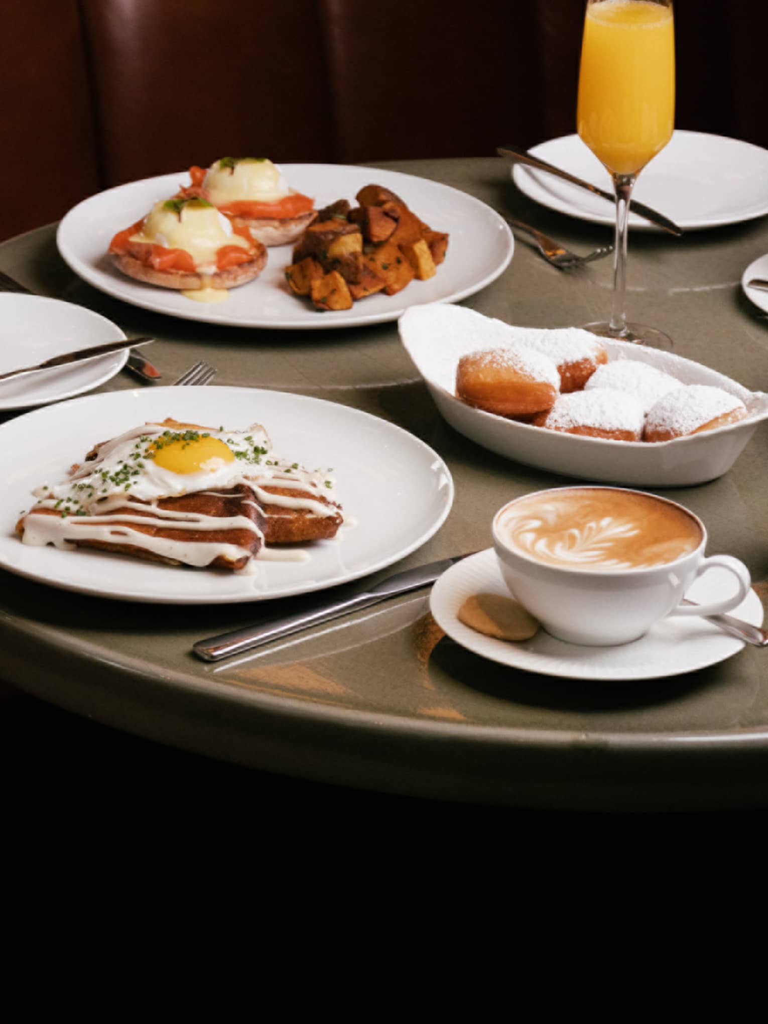 White dishes of brunch dishes and mimosa flute on round grey table