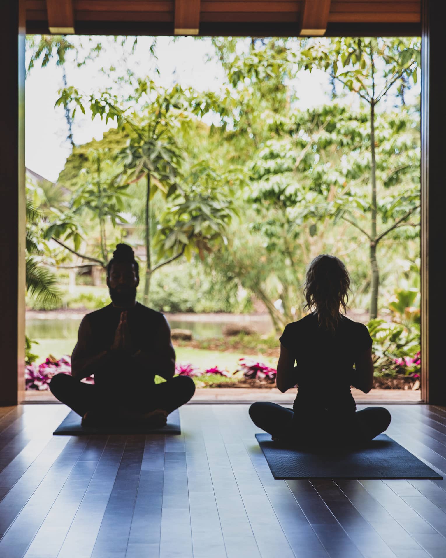 Two people practice yoga in the outdoor covered pavilion surrounded by greenery