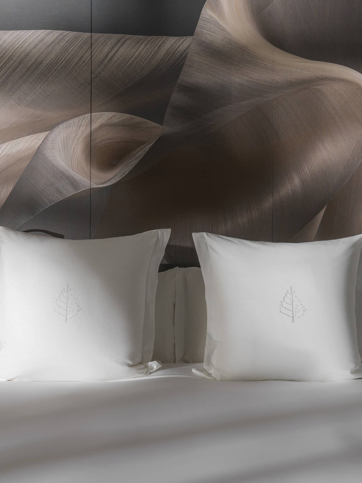 Close-up of a Four Seasons king bed with white pillows and soft lighting, flanked by bedside tables holding white flower arrangements