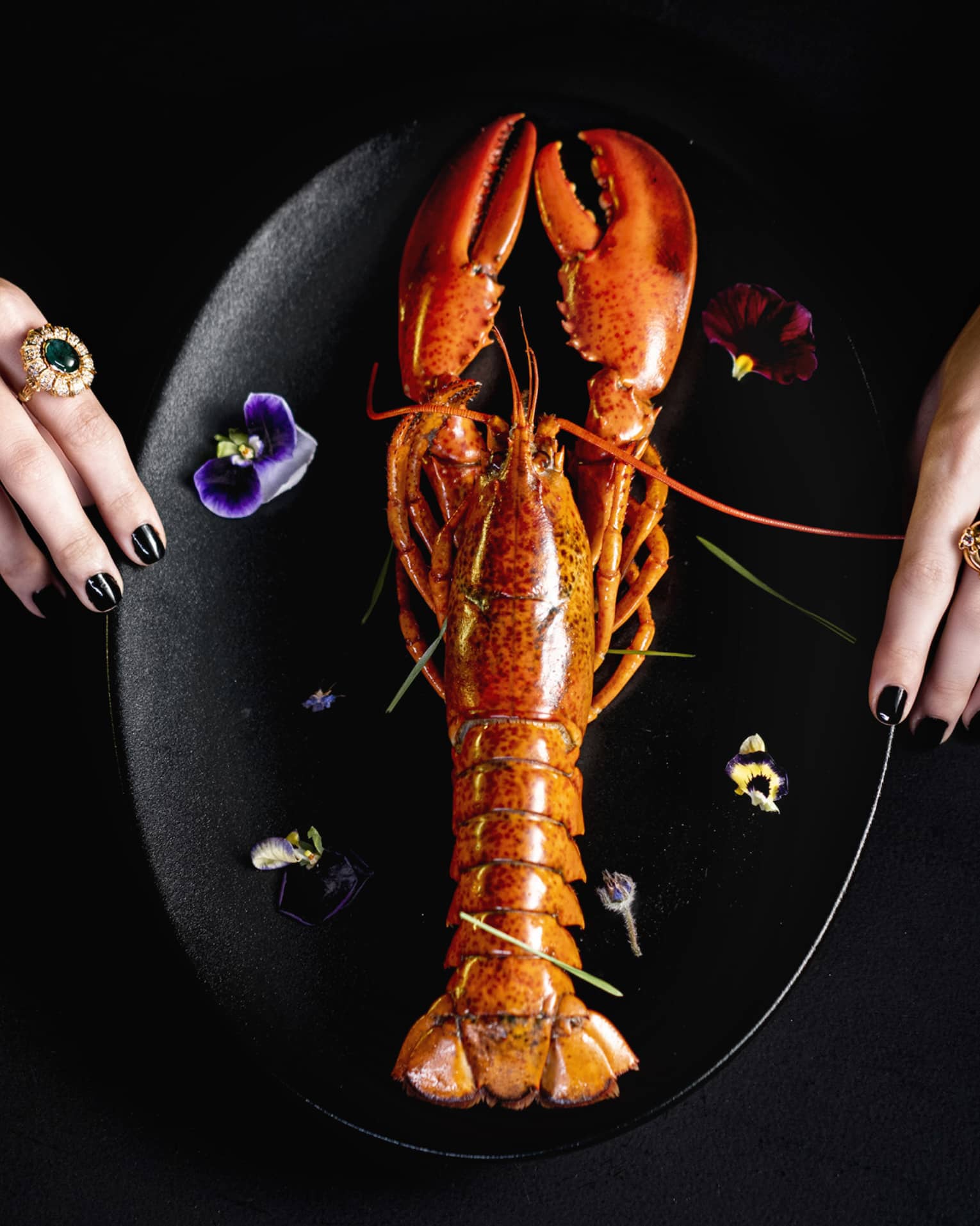 Whole lobster plated vertically on black plate with garnish