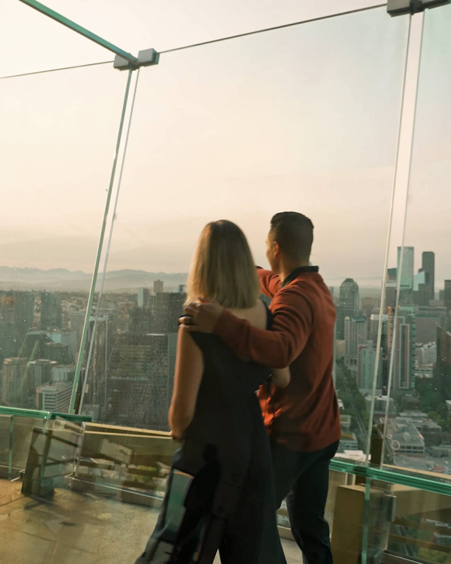A man and woman walking in a tall building with glass walls looking out at a city.