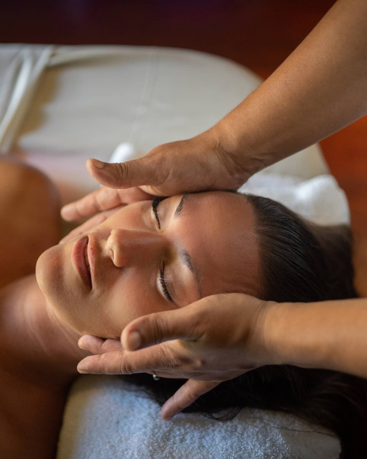 Woman lays on massage table with eyes closed as hands massage her cheeks and chin