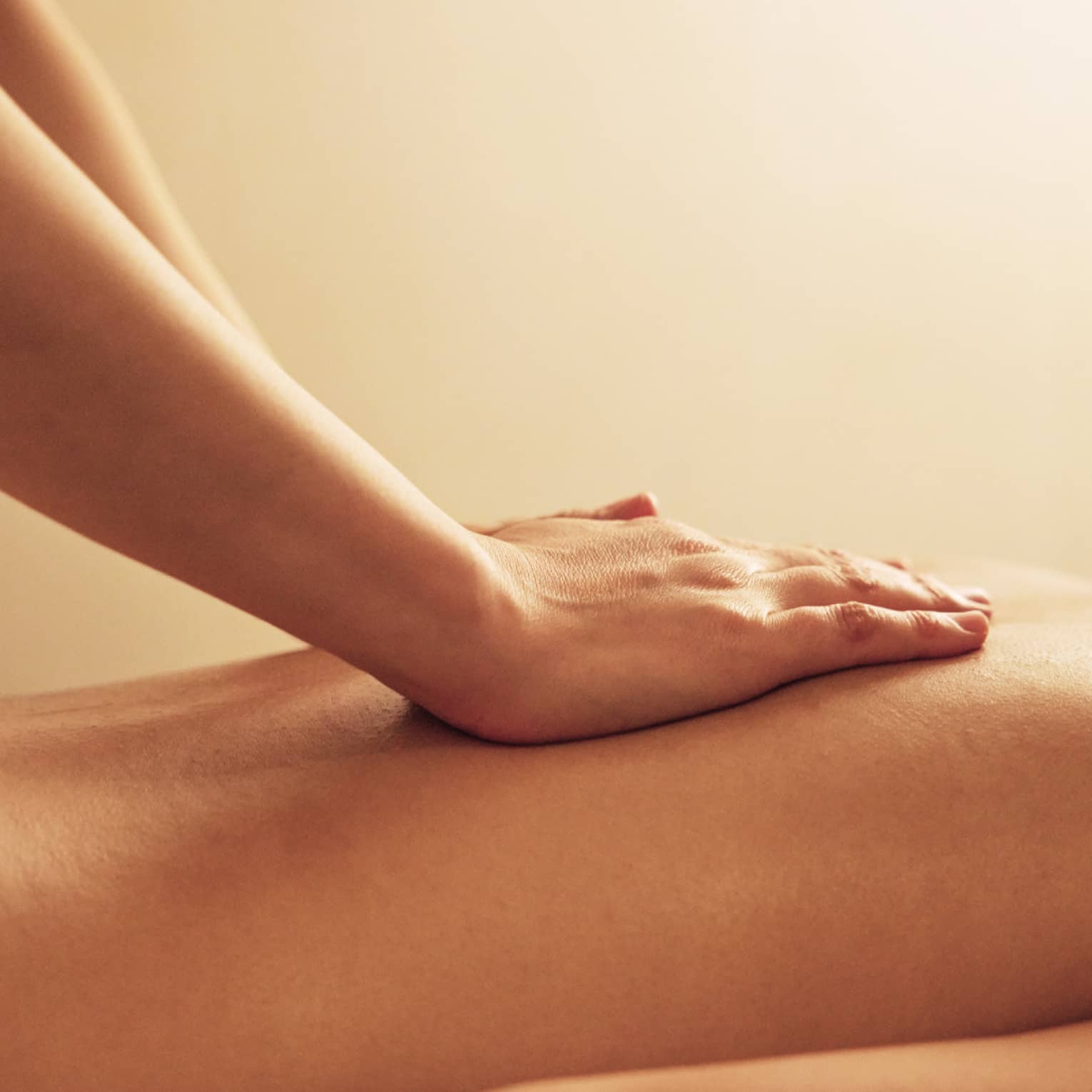 Masseuse rests hands on woman's bare back as she lays on massage table