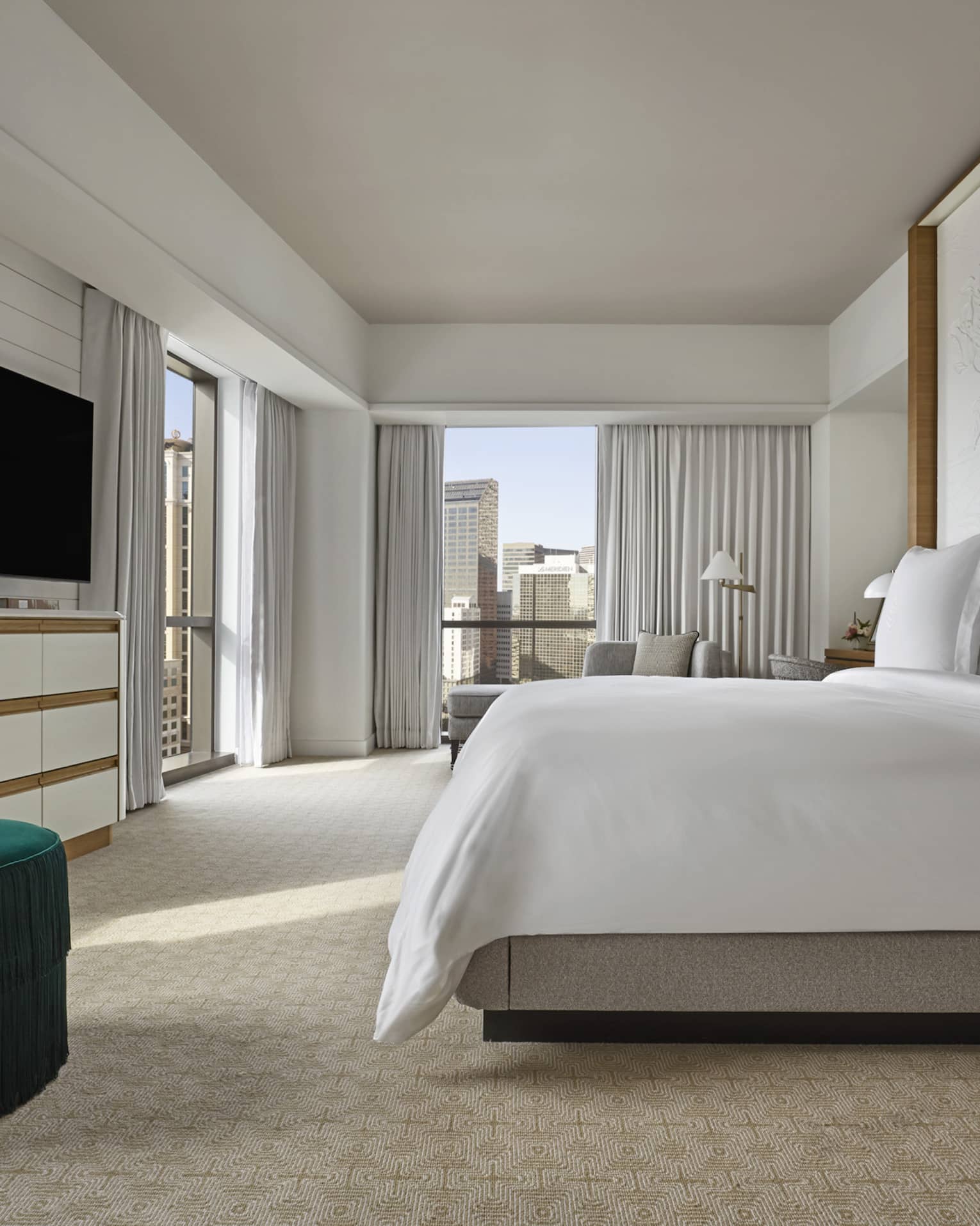 Suite with white king-size bed, flat screen TV, emerald green armchair and floor-to-ceiling windows