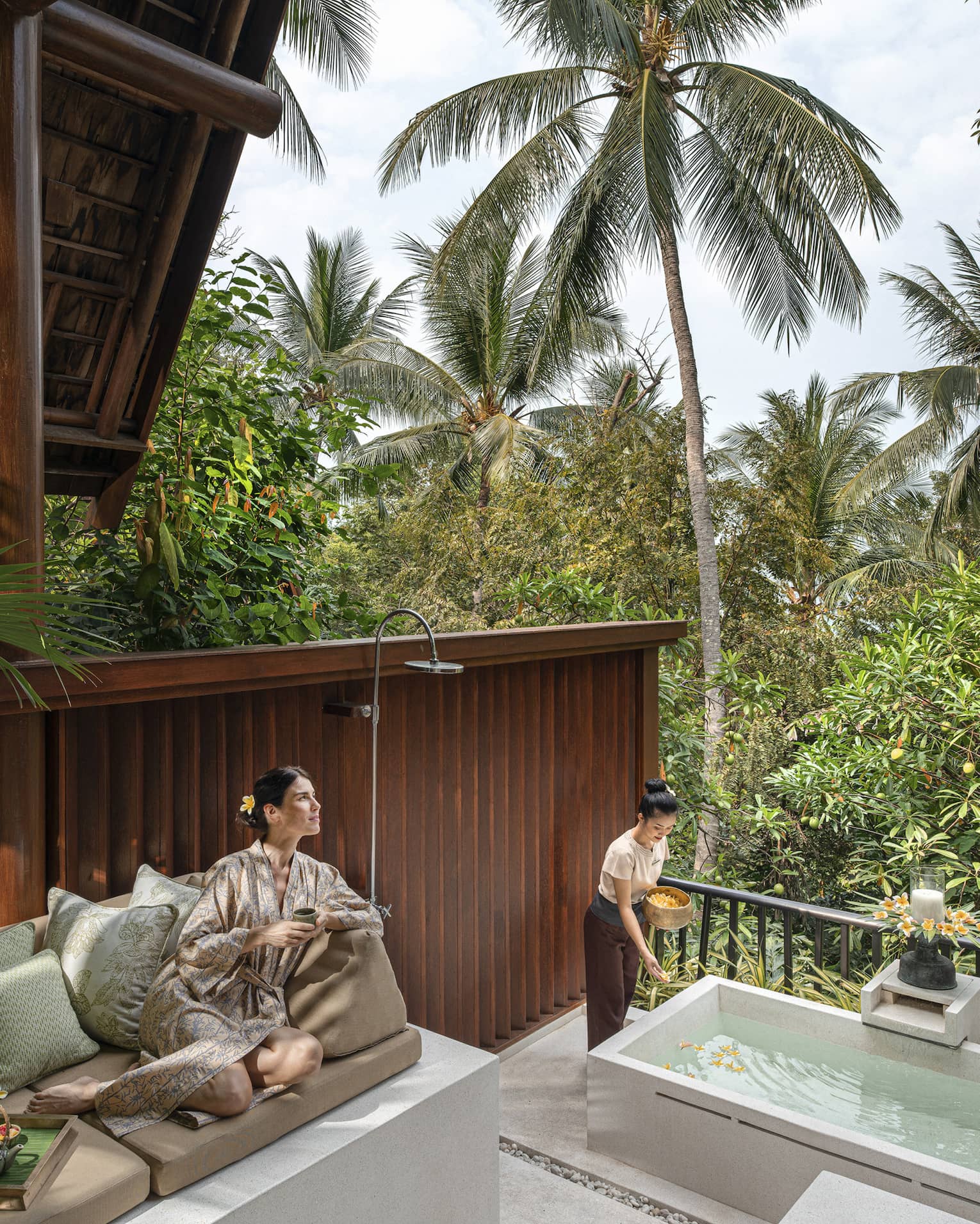 Woman in silk robe lounges on outdoor sofa at the resort spa amidst the lush green garden.