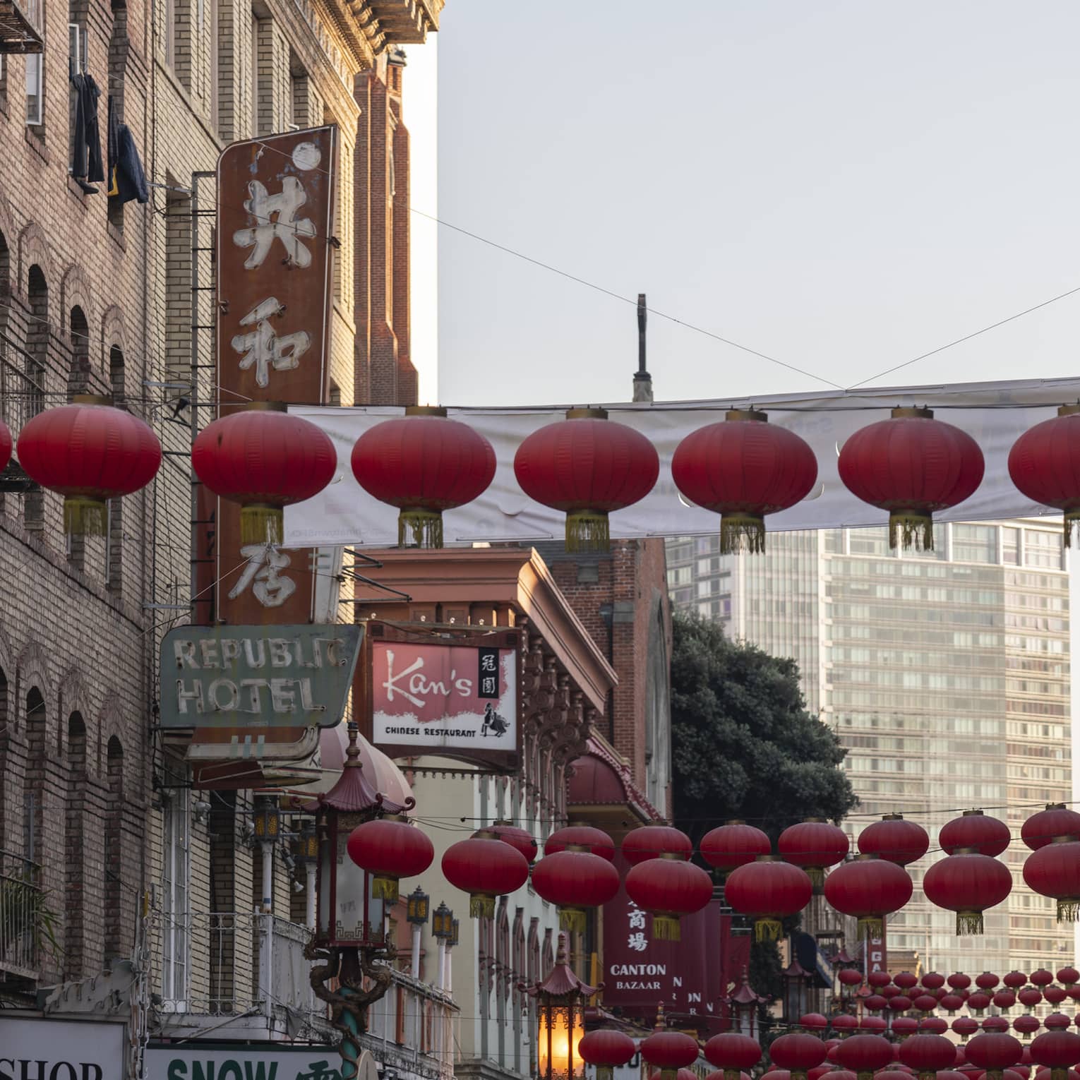Strings of red lanterns hang across a street in the heart of Chinatown with business signs in English and Chinese characters.