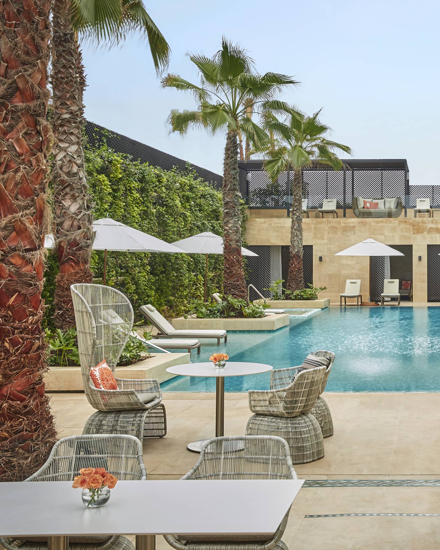 Courtyard pool flanked by tables and chairs with umbrellas, palm trees