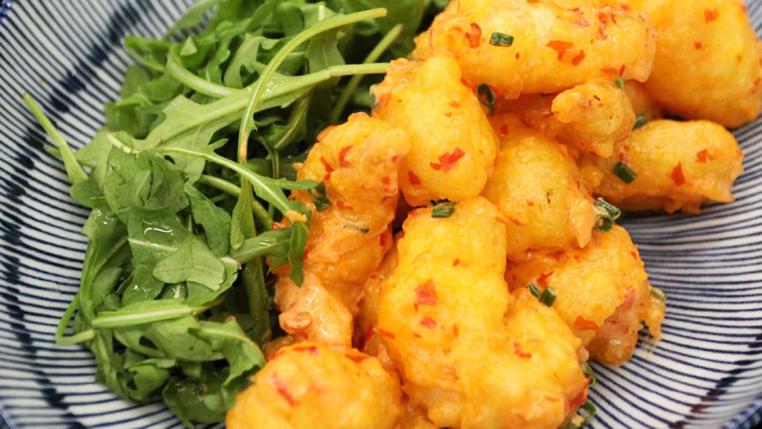 Close-up of shrimp tempura beside green lettuce on black-and-white striped dish