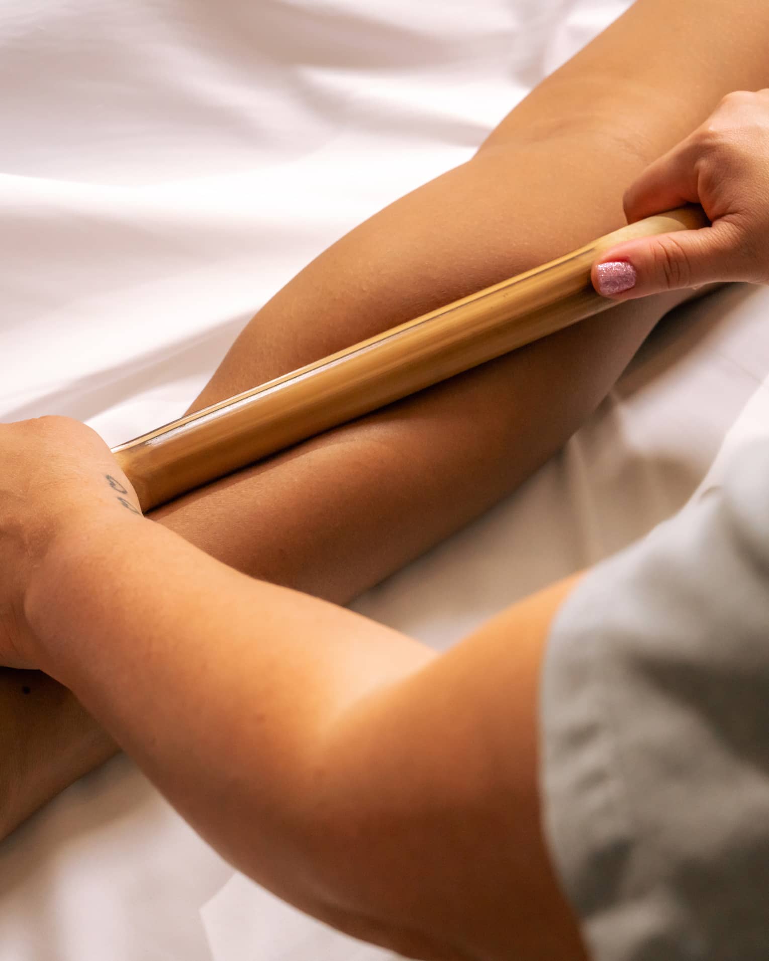Pair of hands rolling a bamboo stick over a person's calf muscle