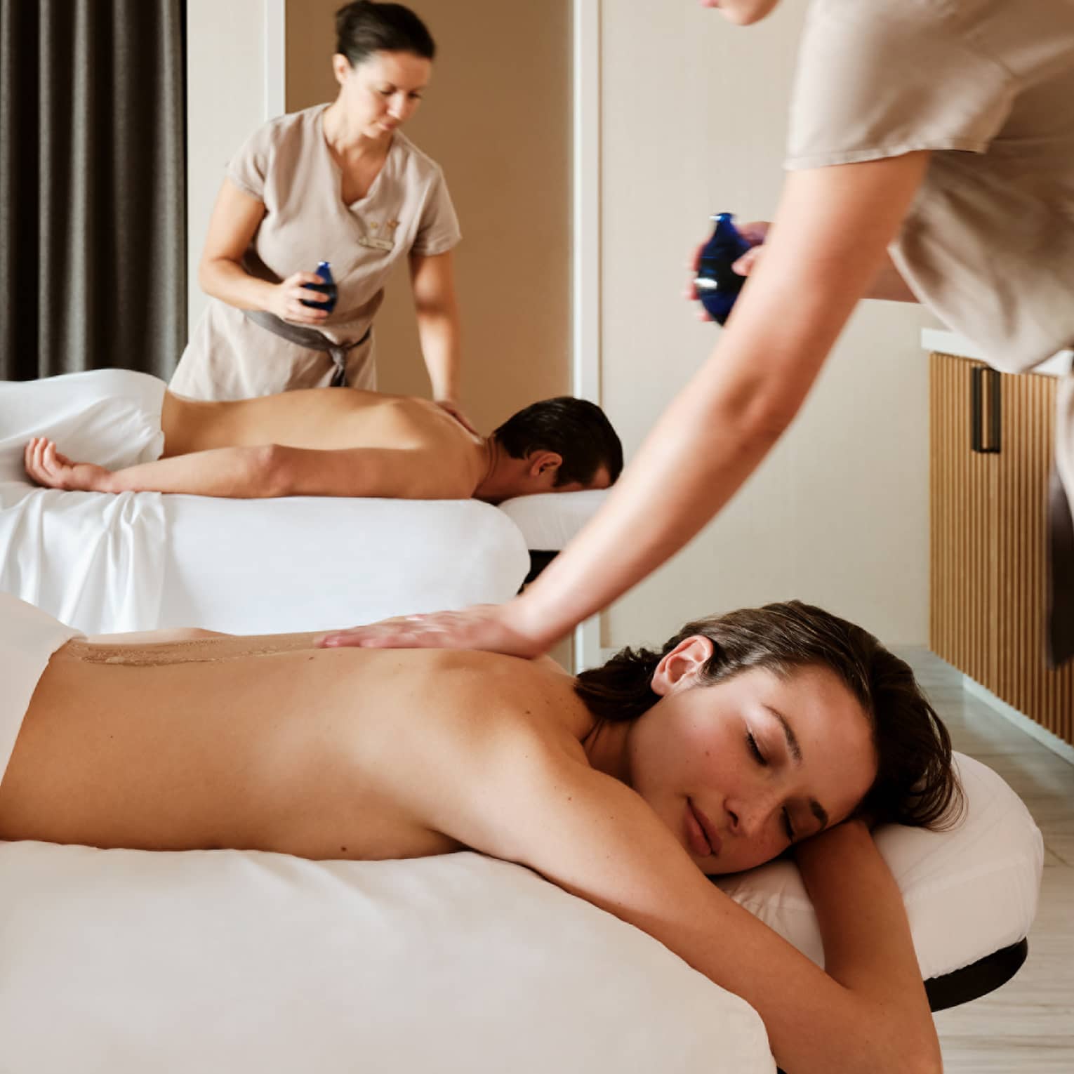 Couple lying prone on spa tables while being massage by spa therapists
