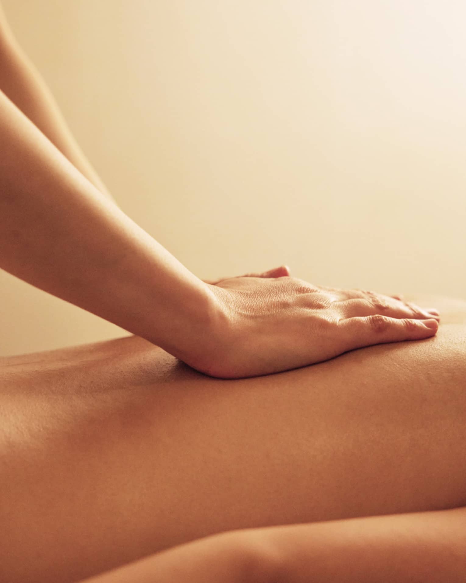 Masseuse rests hands on woman's bare back as she lays on massage table