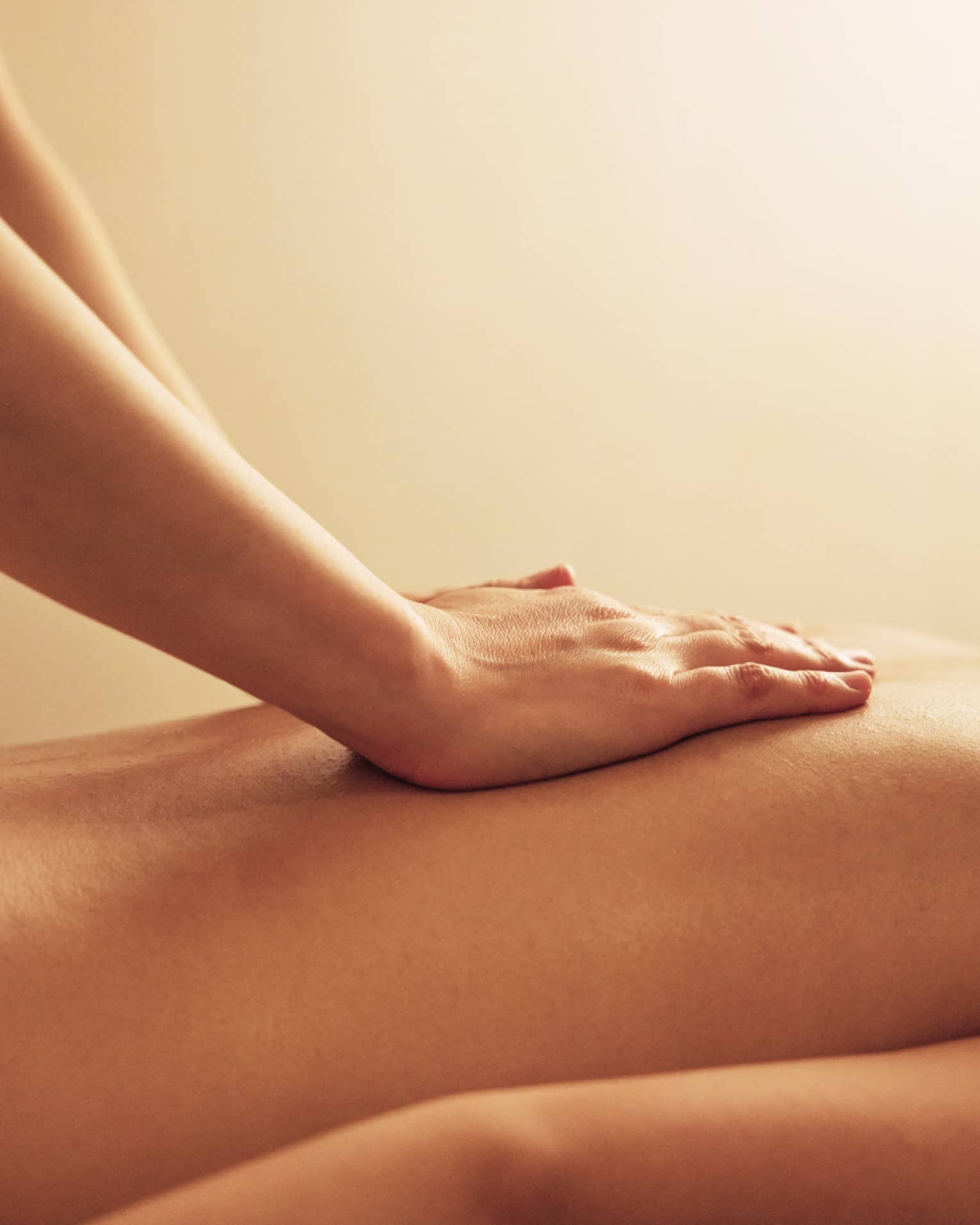 Masseuse rests hands on woman's bare back as she lays on massage table