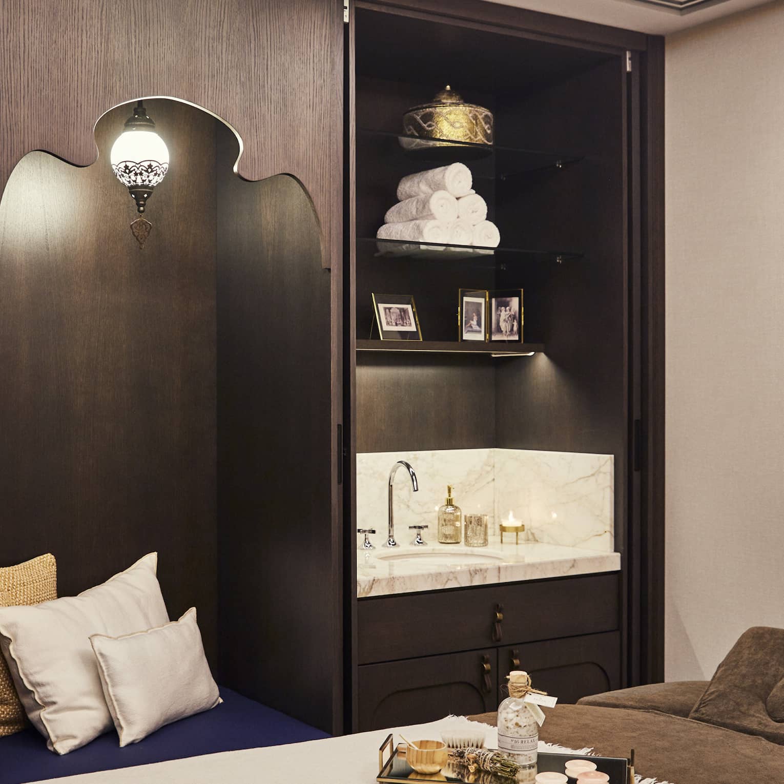 Kuma Spa treatment bed with tray with oils next to large wood cabinet with pillows and sink