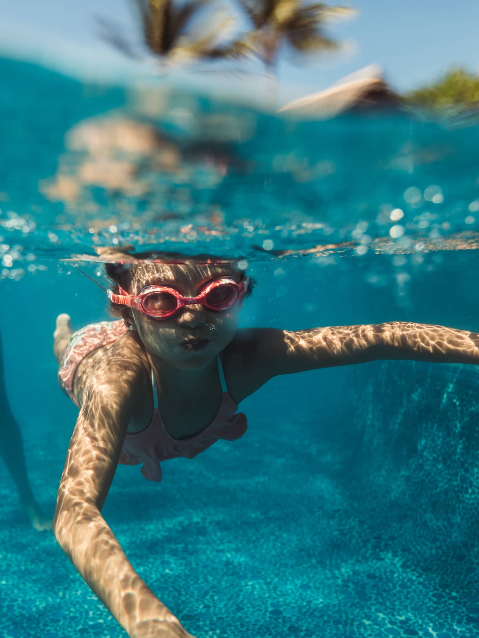A young boy snorkeling in a pool with red goggles on.