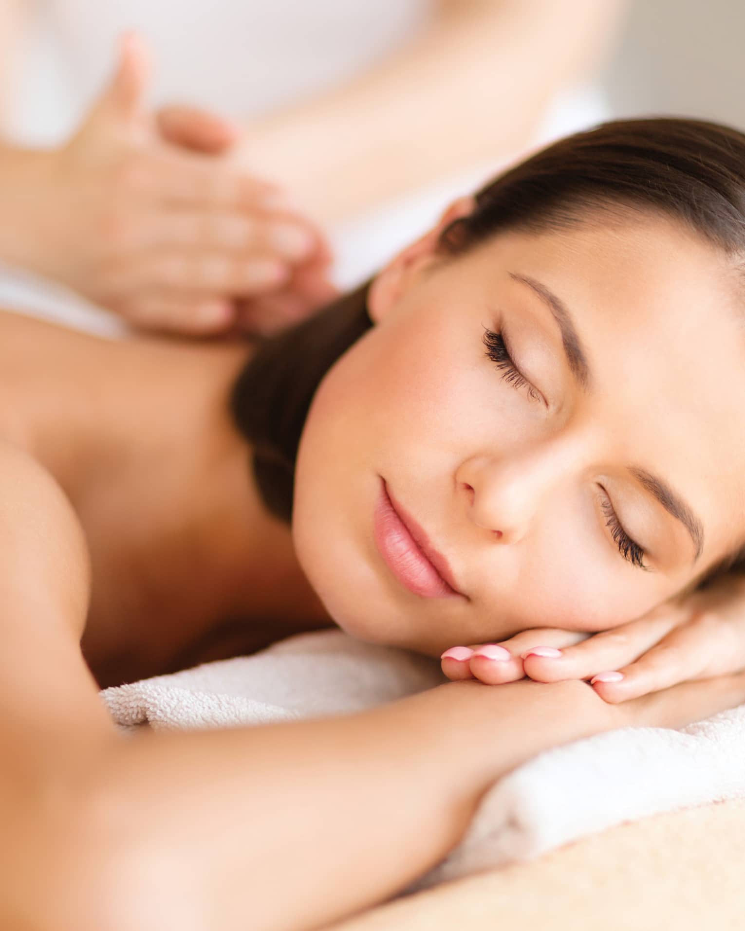 Woman lies on massage table, closes eyes. rests head on arms as spa staff massages back