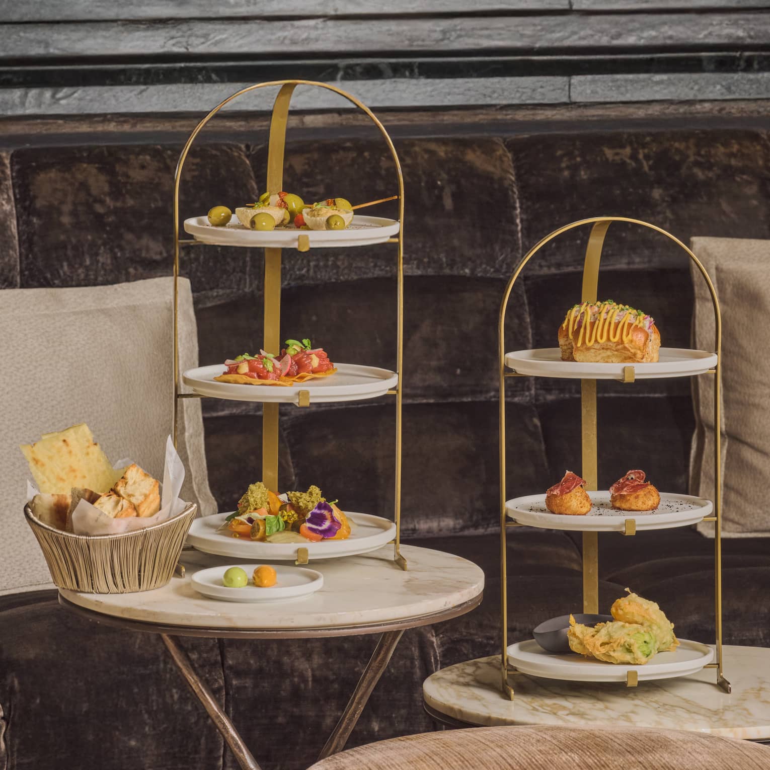 Three-tiered serving stands hold small bites and sit on small round tables in a restaurant setting.