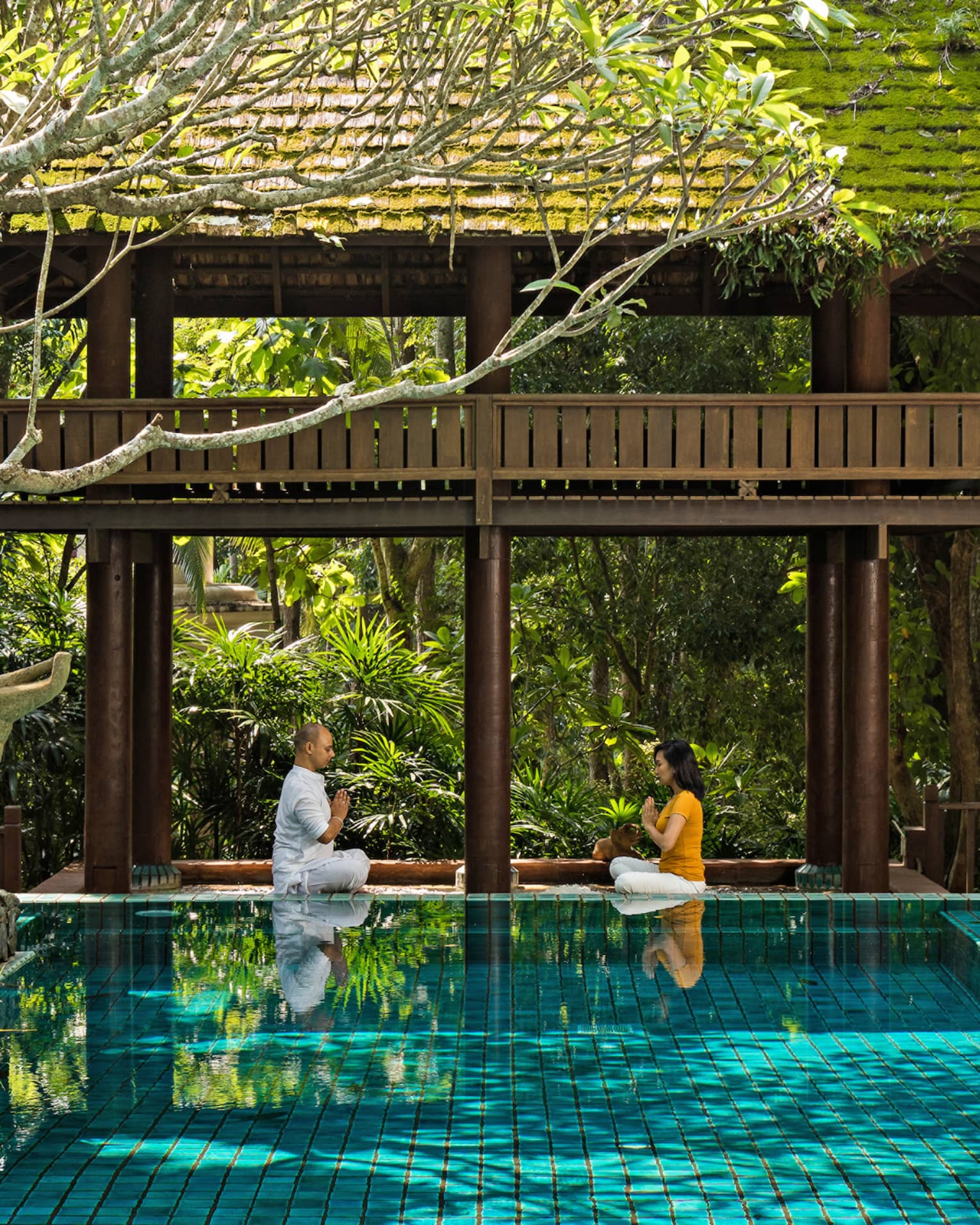 Couple practicing meditation in an outdoor pool setting 
