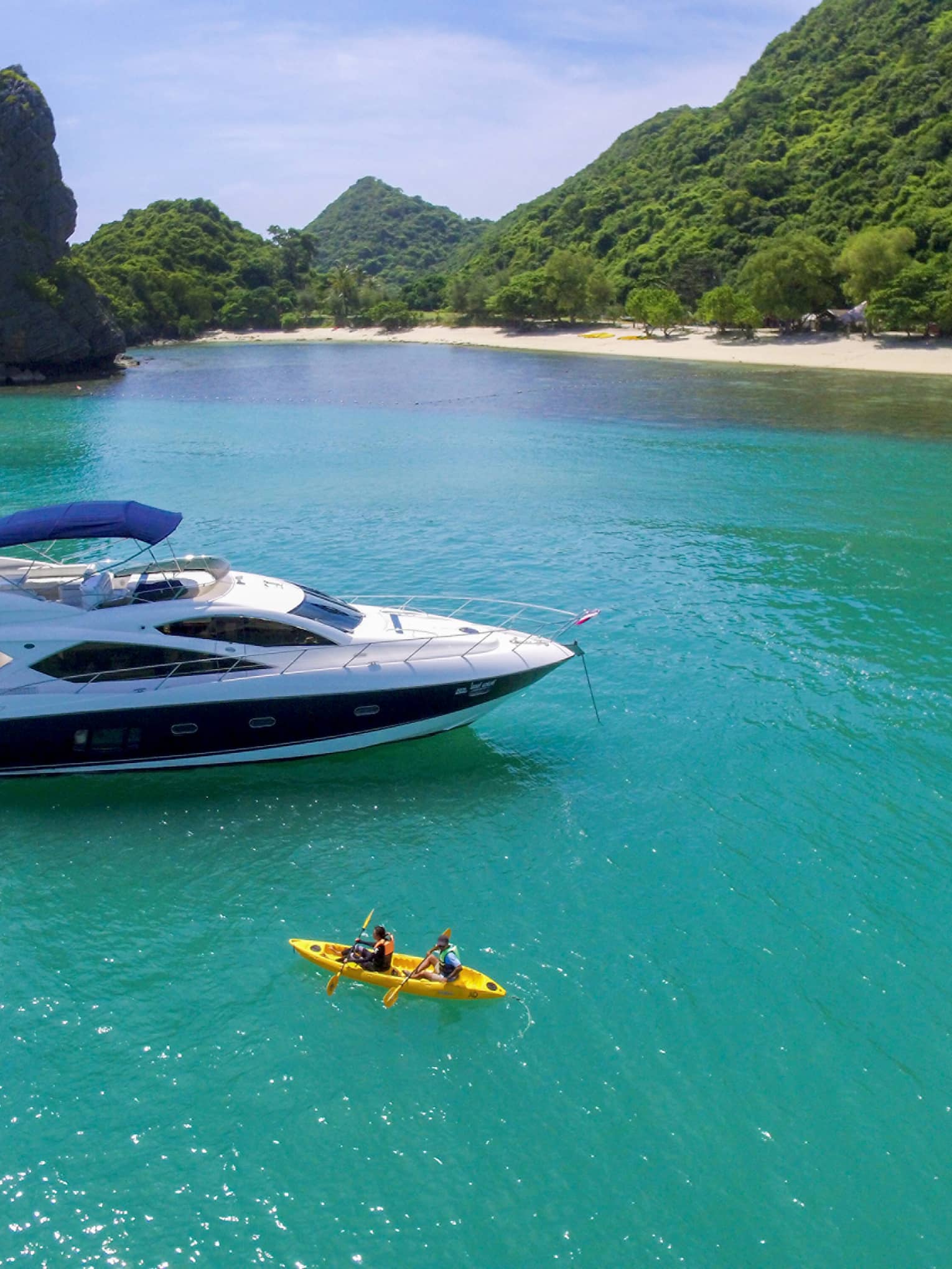 Two people in yellow kayak in front of large white yacht by island in blue ocean