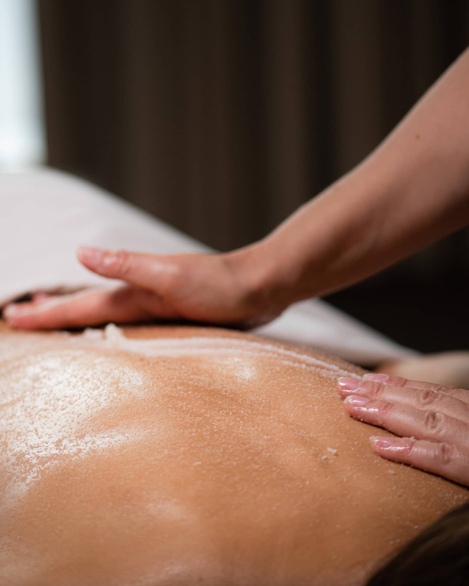 A masseuse spreads a cream across a woman's back as she lies on a massage table.