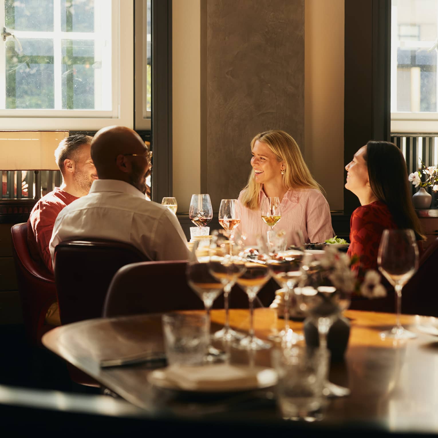 People sitting around a table, enjoying a meal in an indoor dining space. The table is next to a window that is letting in bright natural light.