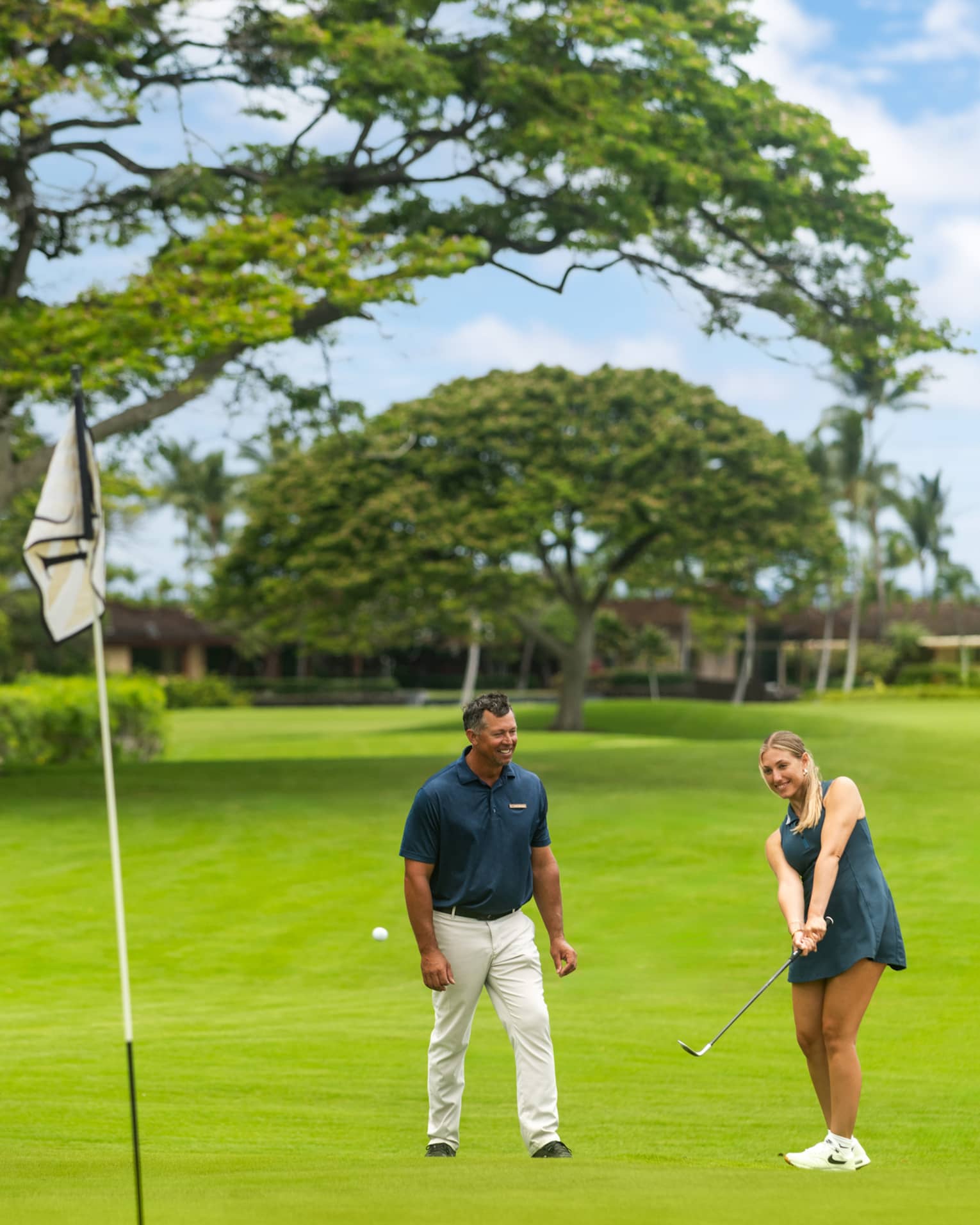 Two people on a golf course with one practicing her short game.