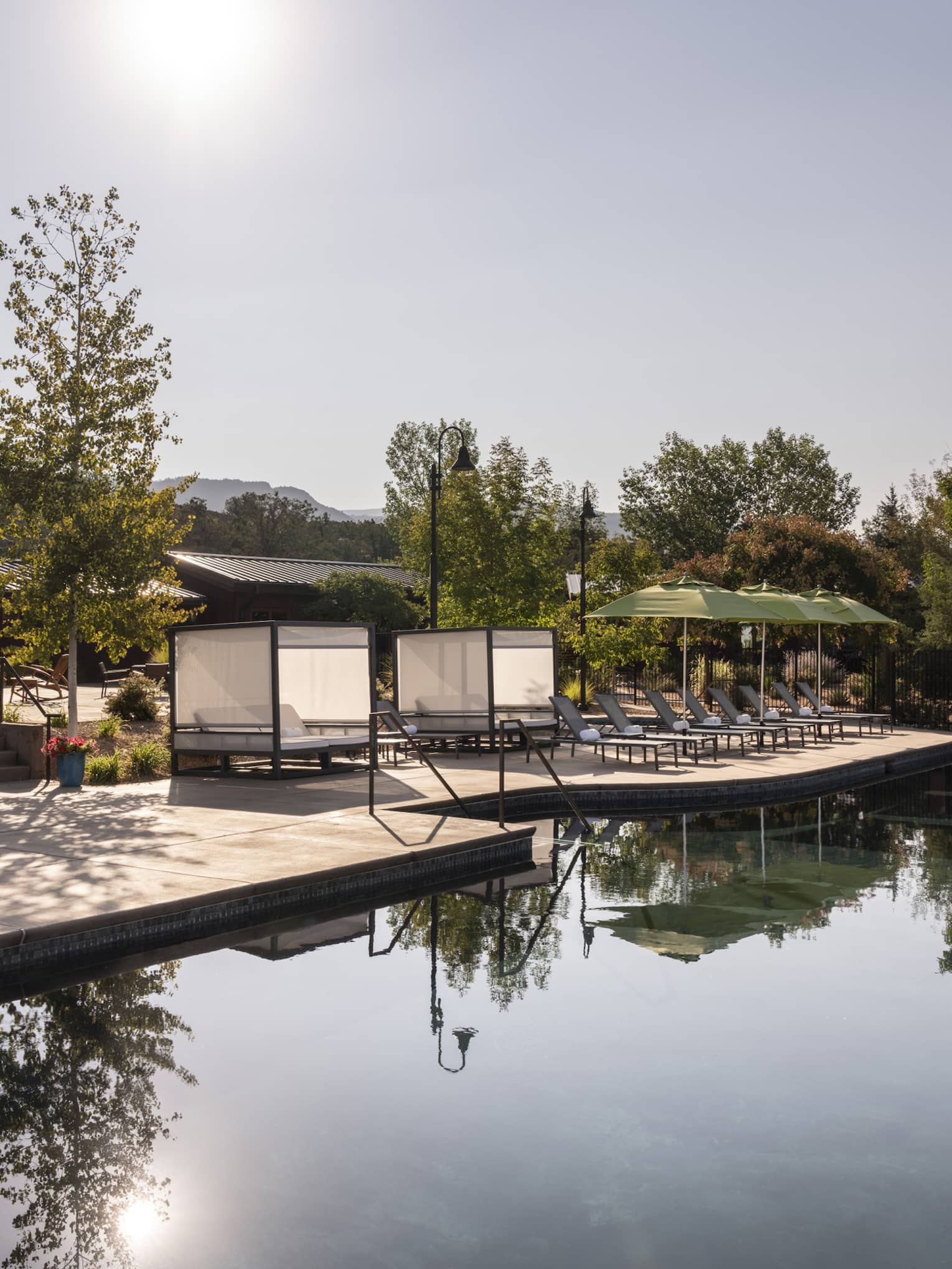 An outdoor pool near trees, lounge chairs, and green umbrellas.