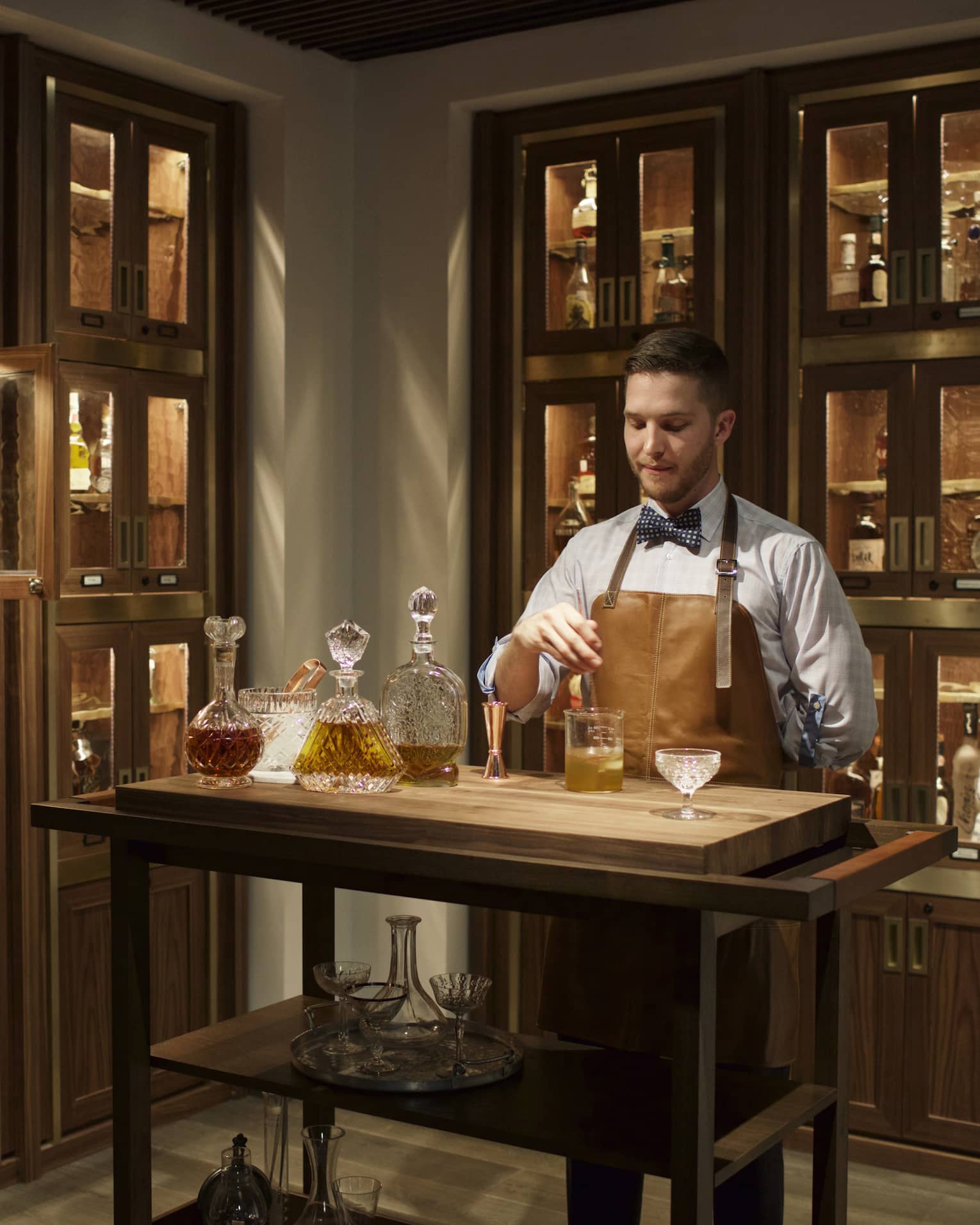 Bayou & Bottle mixologist in apron stirs bourbon cocktail, surrounded by illuminated display cases with bottles 