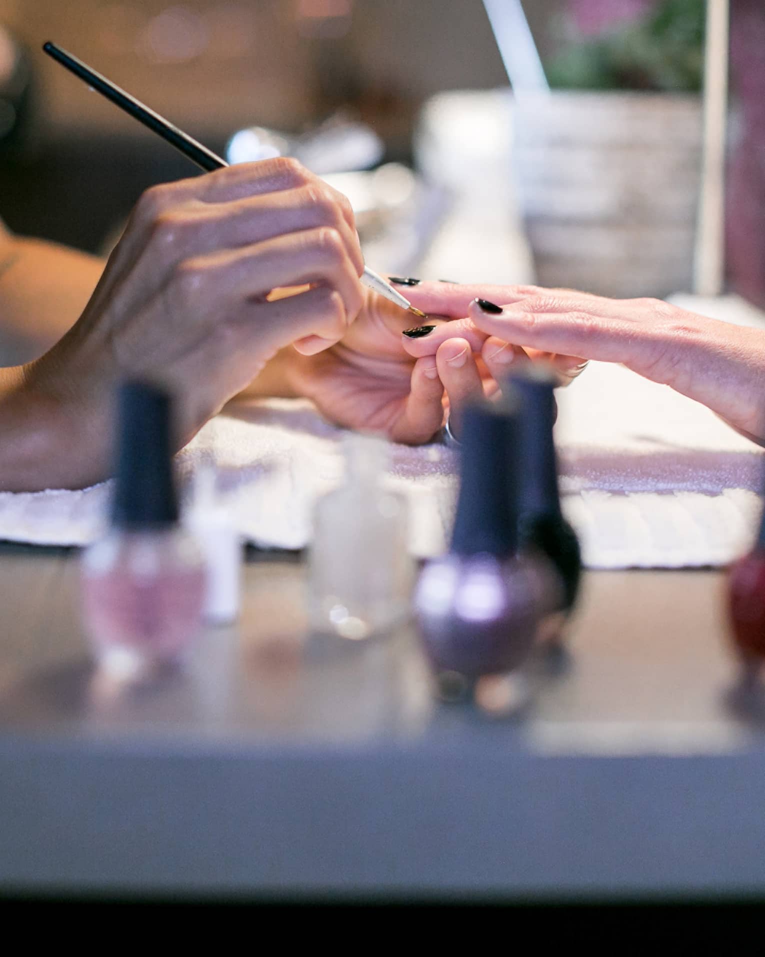 Close-up of spa staff painting woman's nails at manicure table