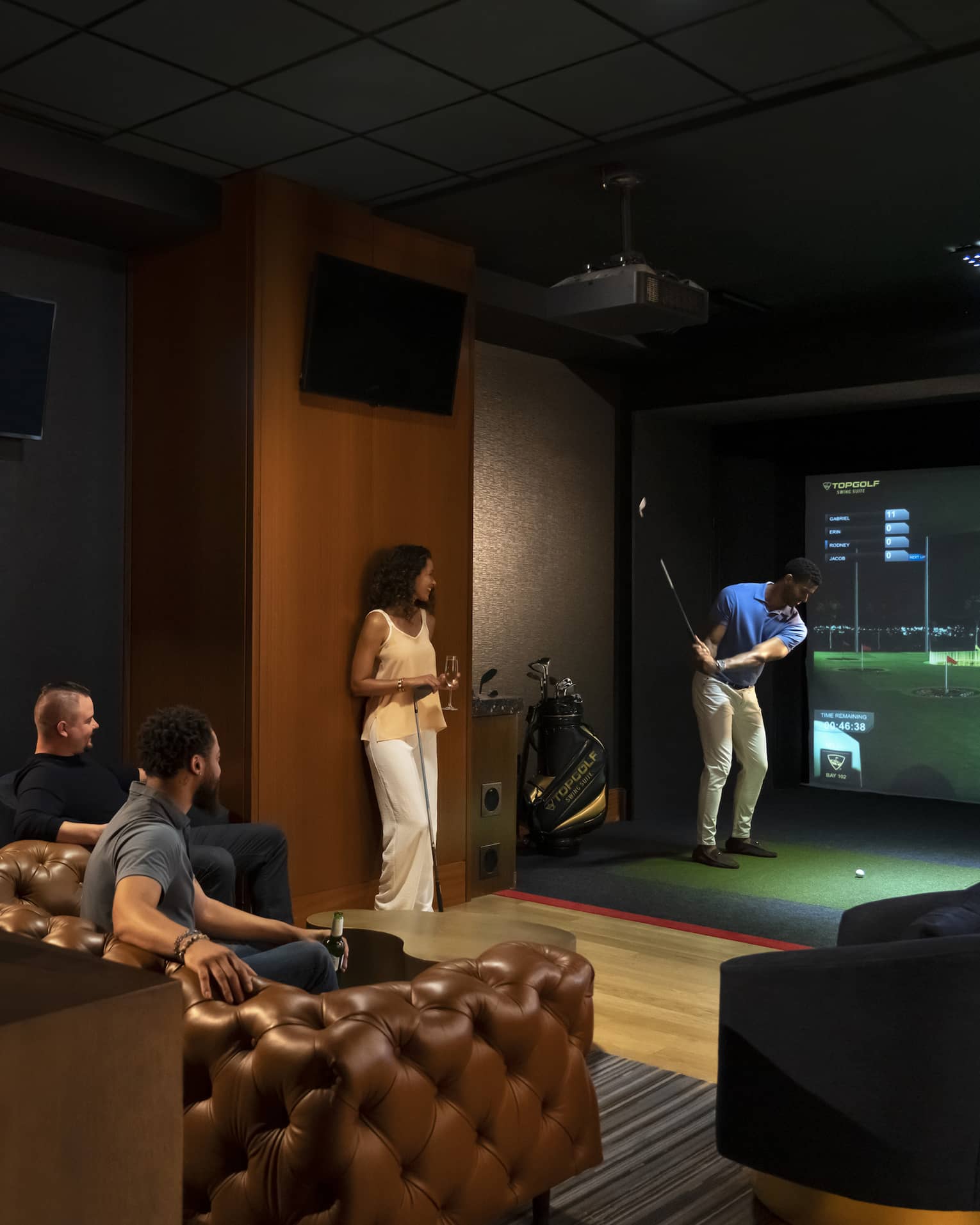 A group of people enjoying an indoor golf simulator experience at the luxury hotel Topgolf Swing Suite, with plush seating and a relaxed atmosphere