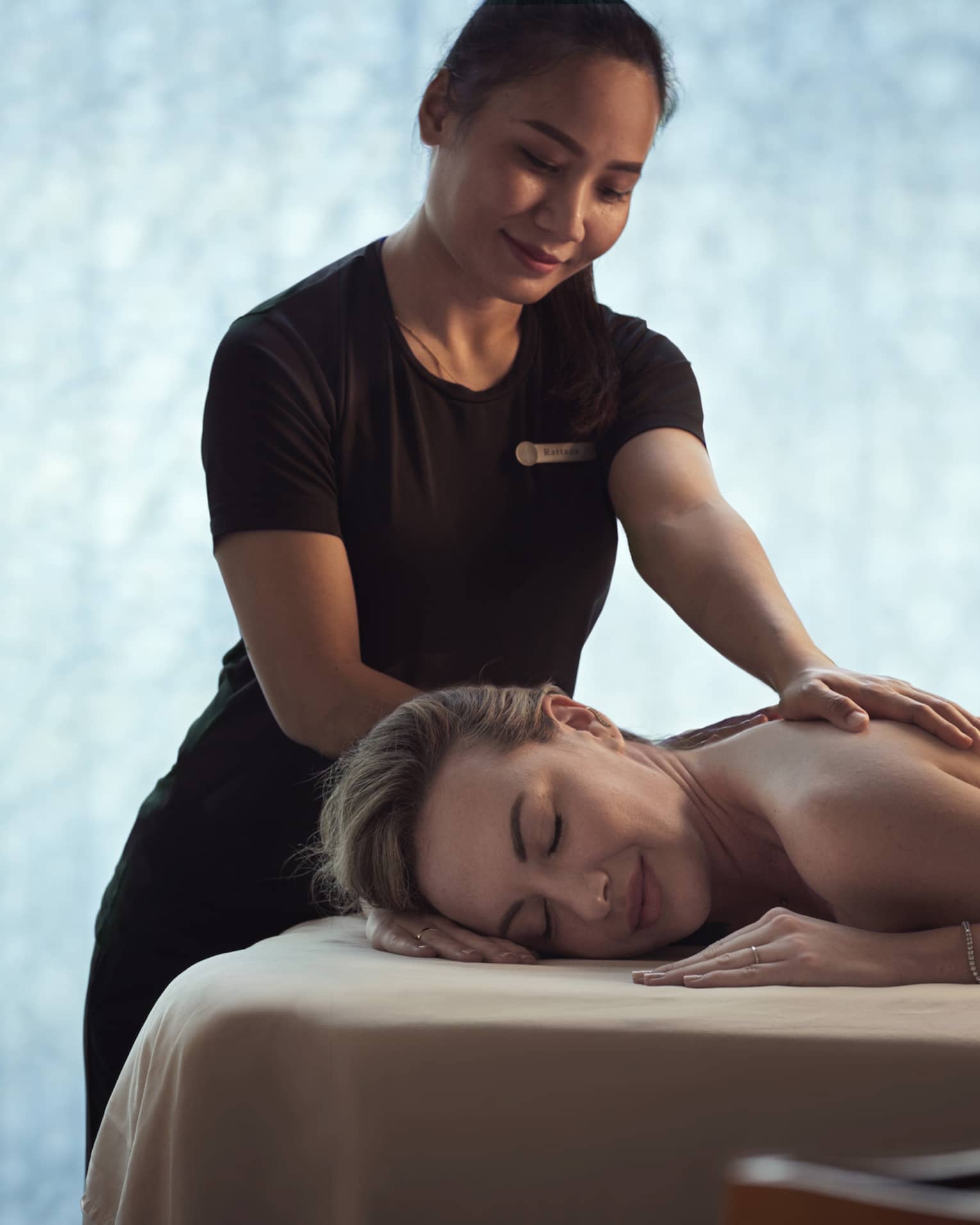 Spa staff massages woman's shoulders as she lays on bed in dark room