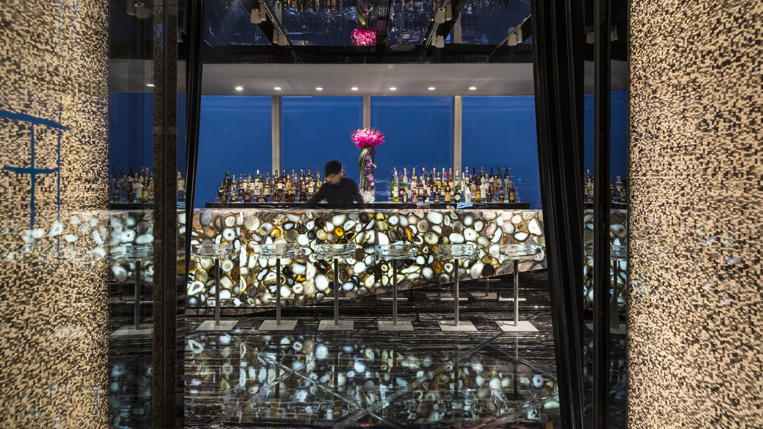 Tian Bar bartender behind bar with illuminated multi colored agate stone, modern clear stools