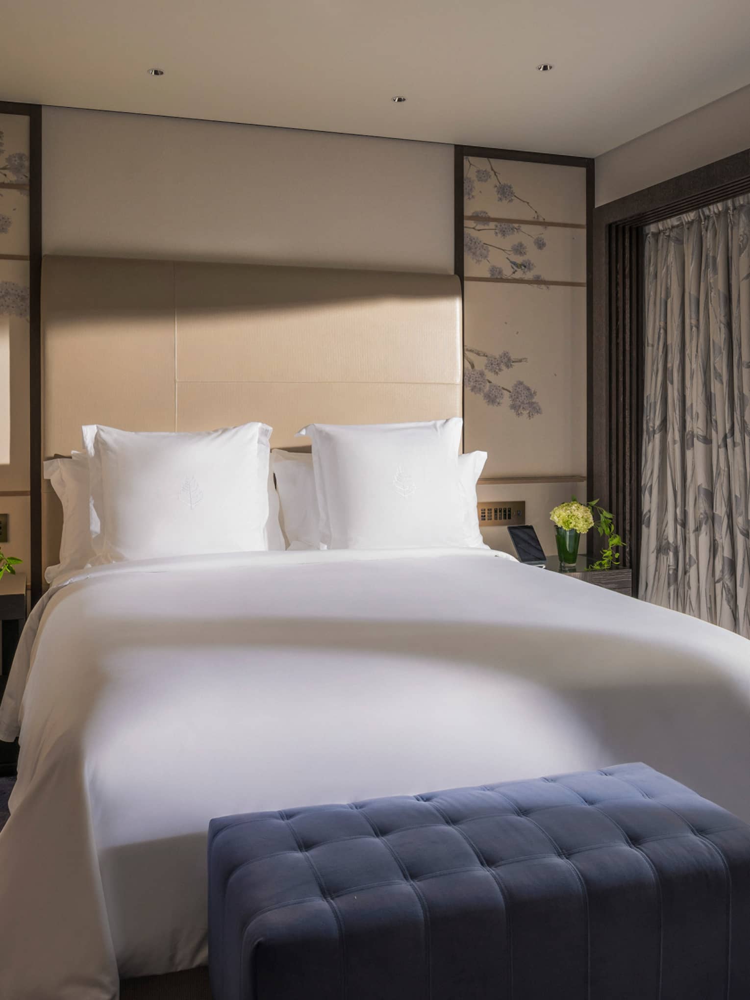 Bright bedroom with a king-size bed, a blue tufted bench and sliding glass doors opening to a private terrace with garden view