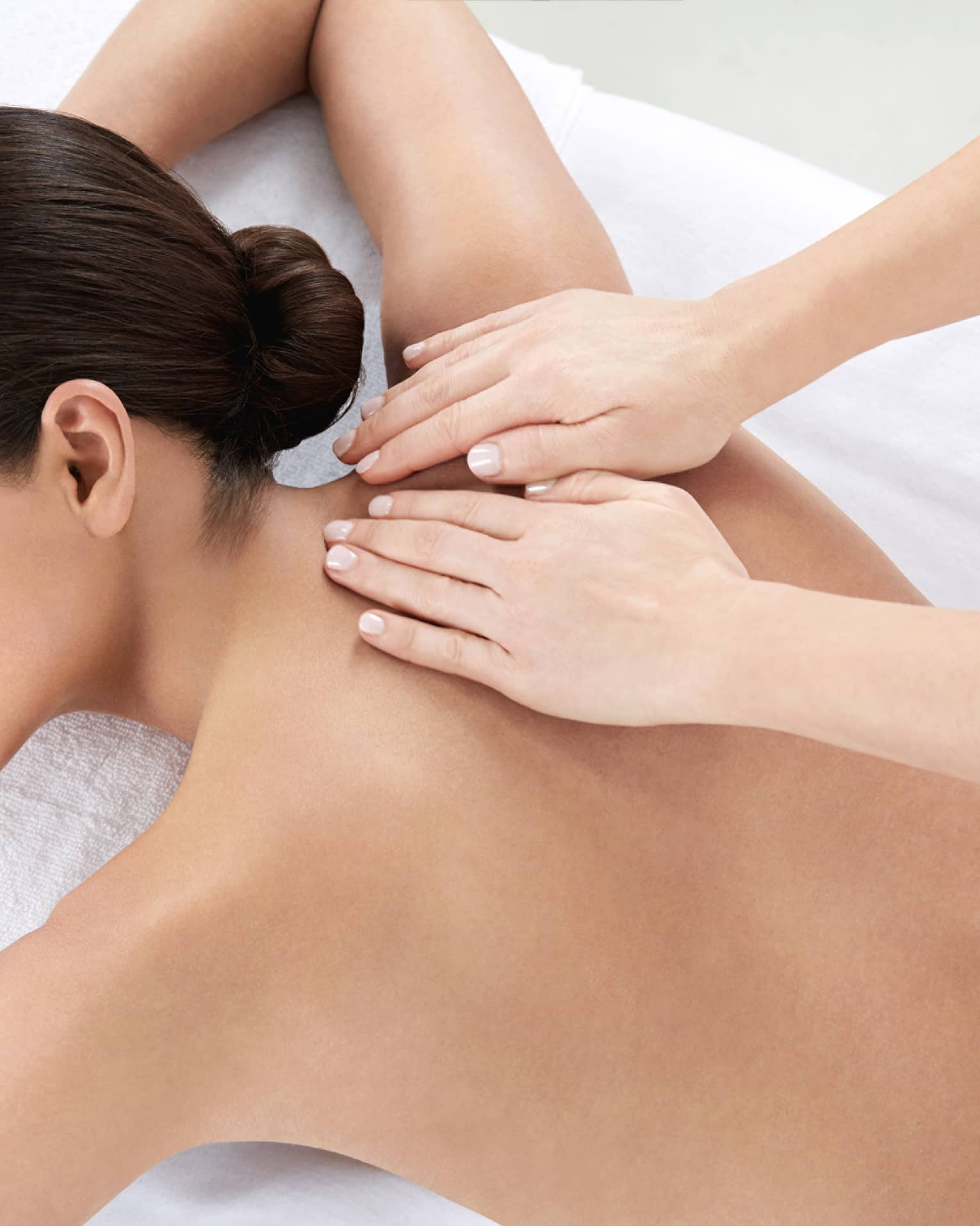 Woman smiles, lies on massage table as hands massage bare shoulders